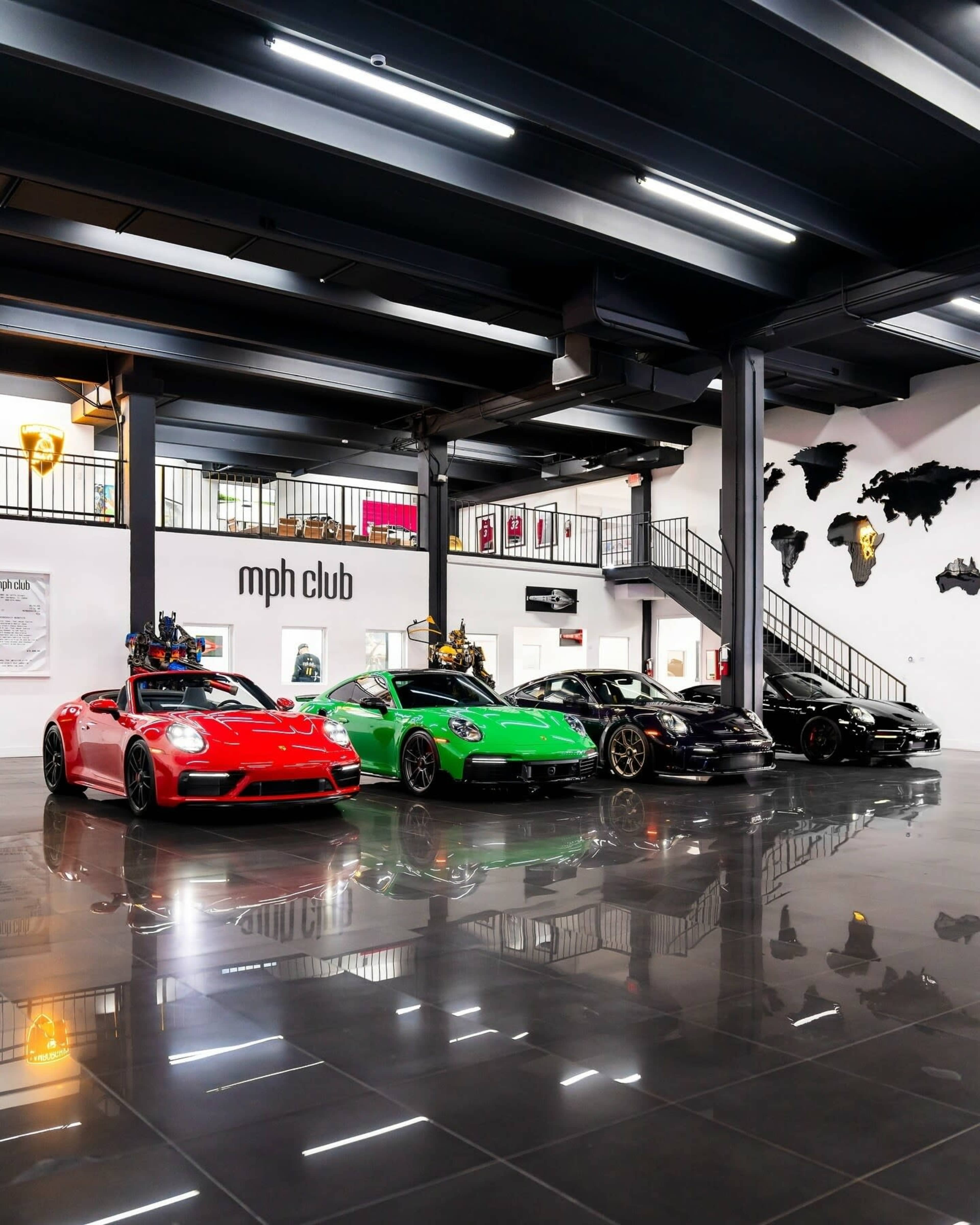 A row of luxury sports cars in various colors is displayed in a modern showroom with a polished floor and art on the walls.