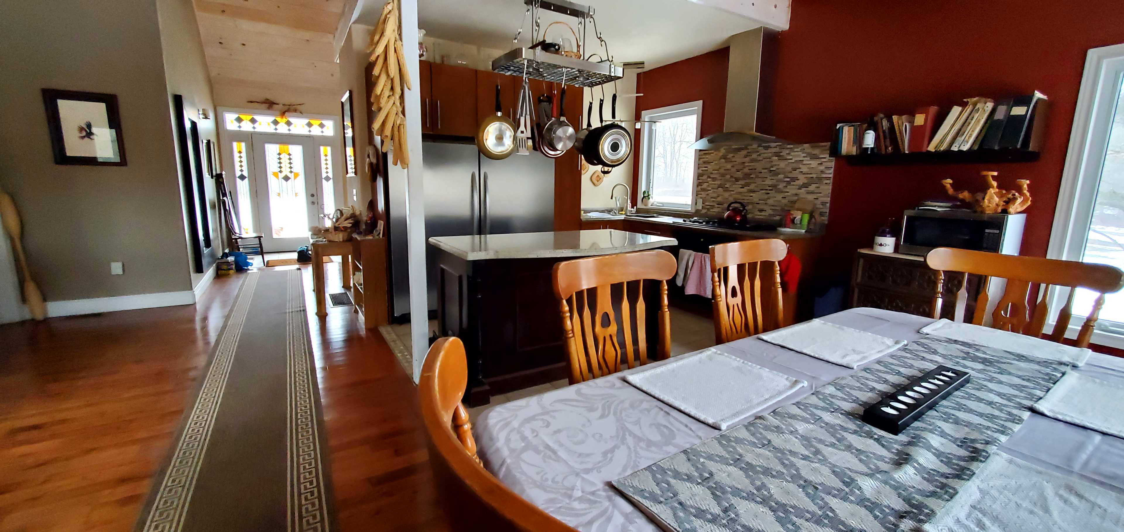 A well-lit kitchen and dining area featuring wooden furniture, a dining table set with placemats, and a modern kitchen with an island and open layout.