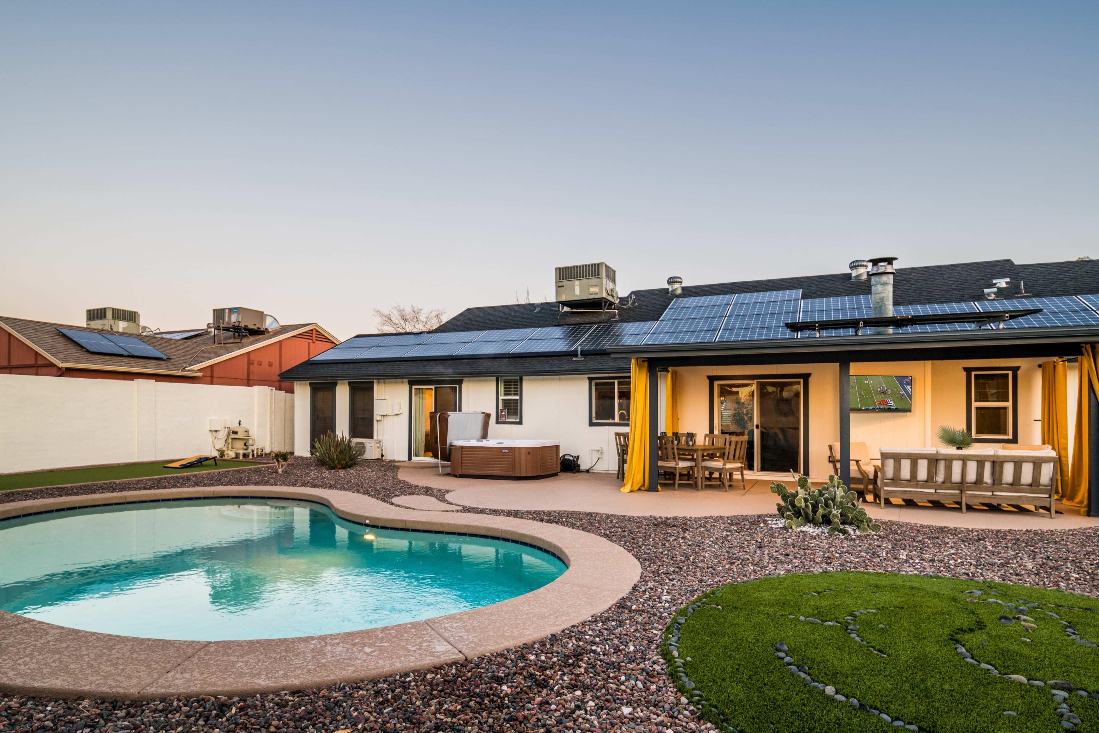 The image shows a backyard with a swimming pool, a hot tub, outdoor seating, and a house equipped with solar panels.