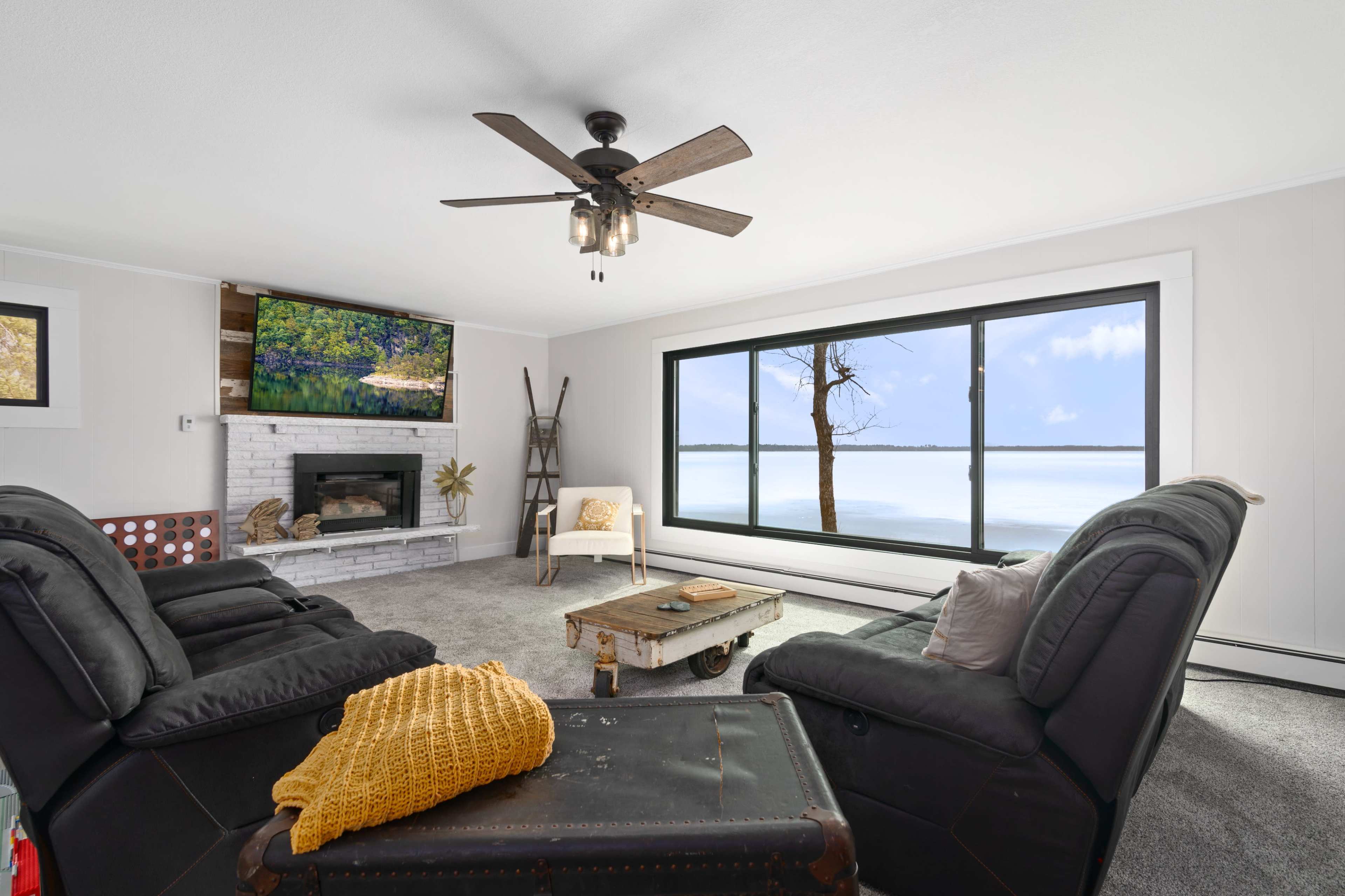 A cozy living room features a sectional couch, a wooden coffee table, and a large window overlooking a serene lake with a bare tree visible outside.