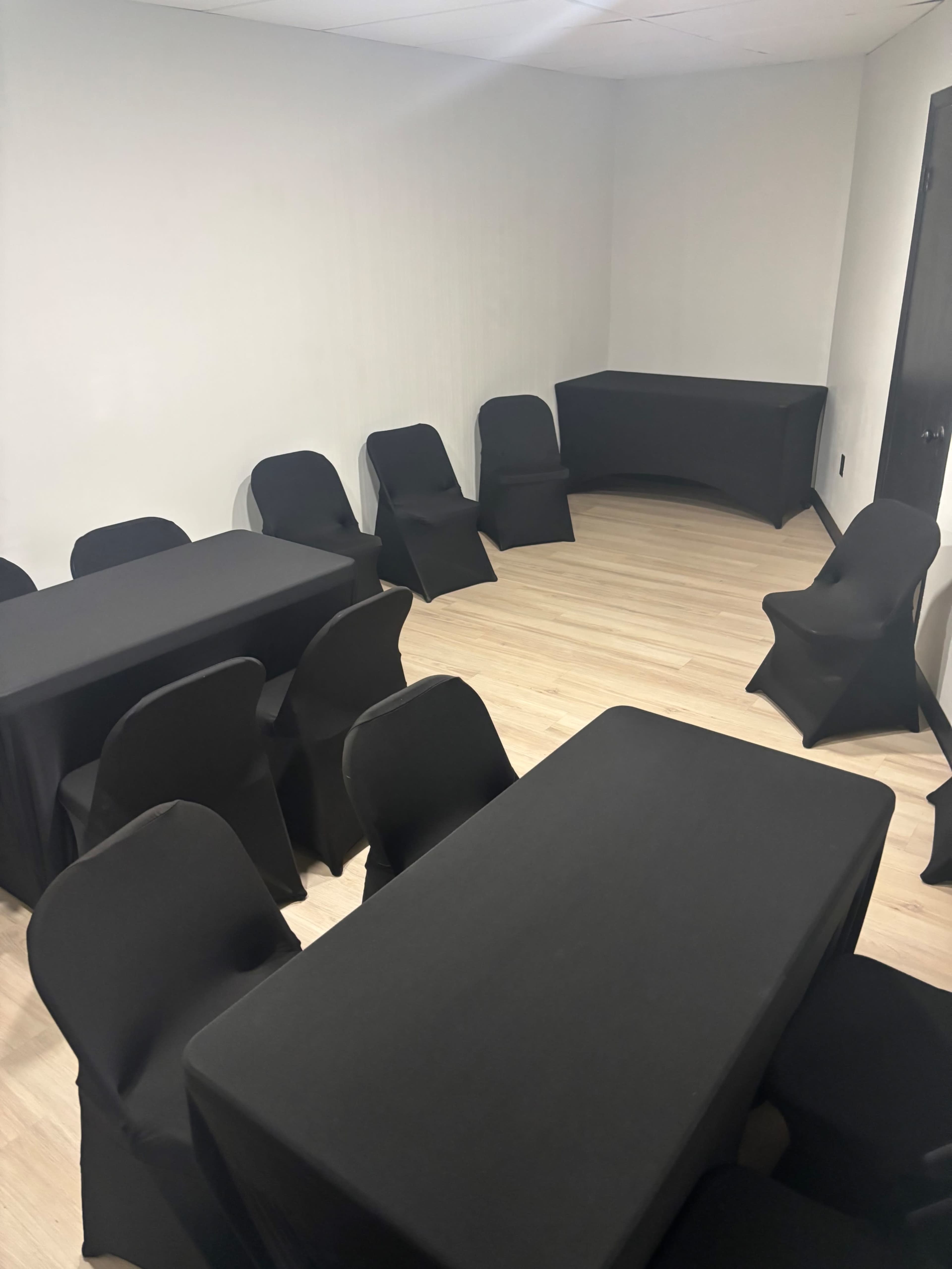 The image shows a conference room with several black-covered tables and chairs arranged around a light wooden floor.