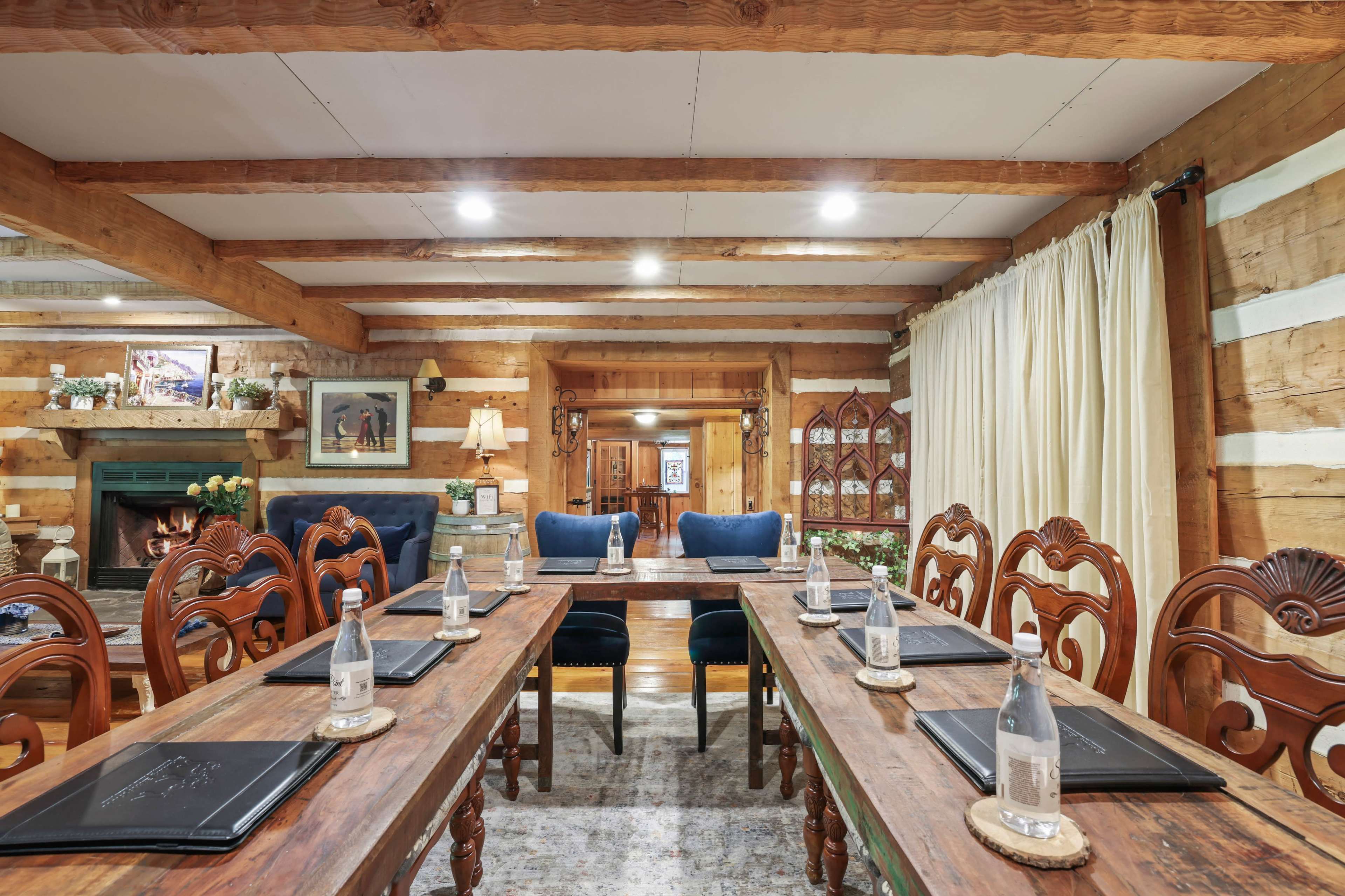 A rustic meeting room with wooden beams, a fireplace, and a long table set with water bottles and menus.