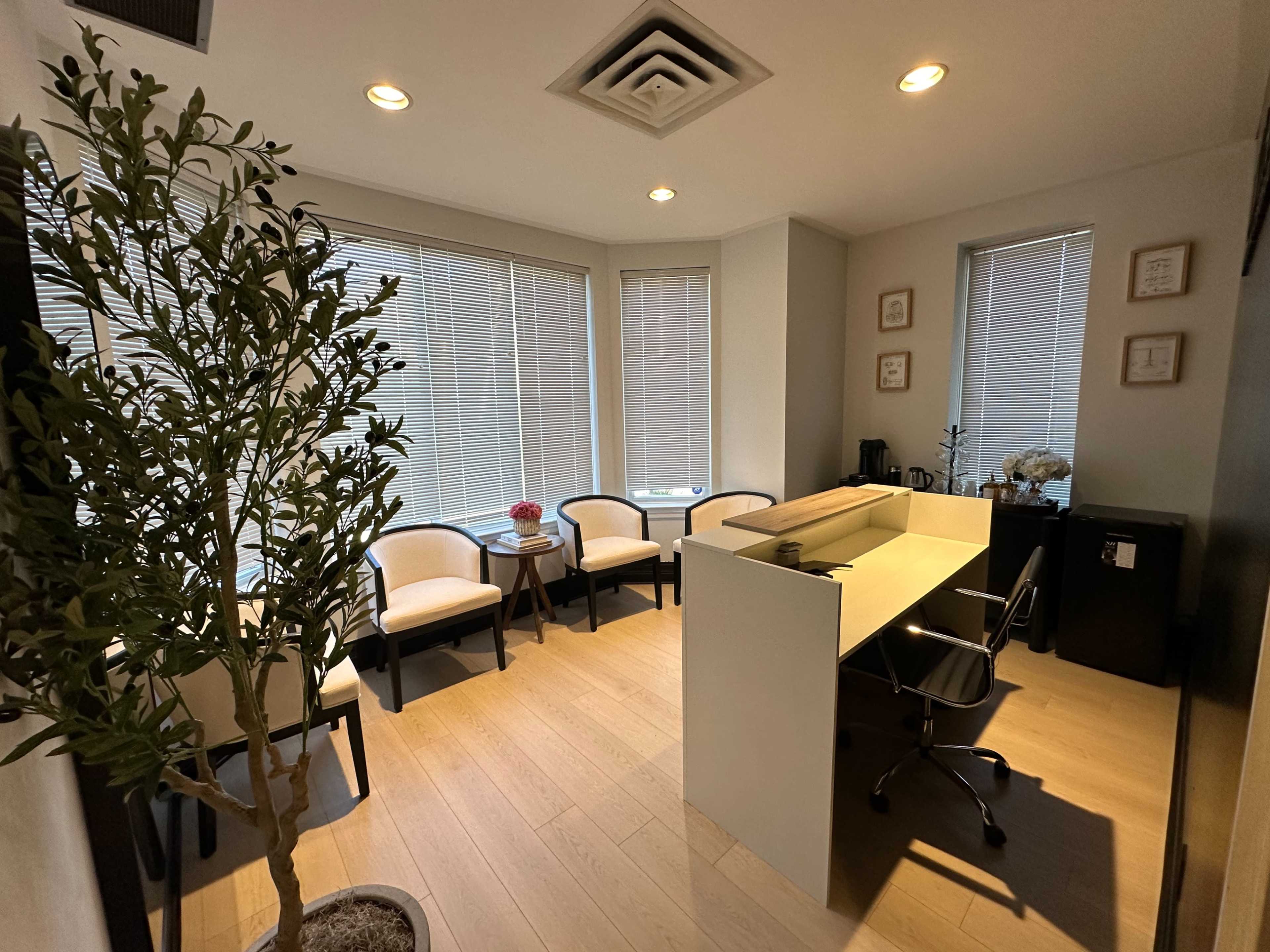 A clean office space with two chairs, a small table, a desk with a computer chair, and a potted plant near the window.