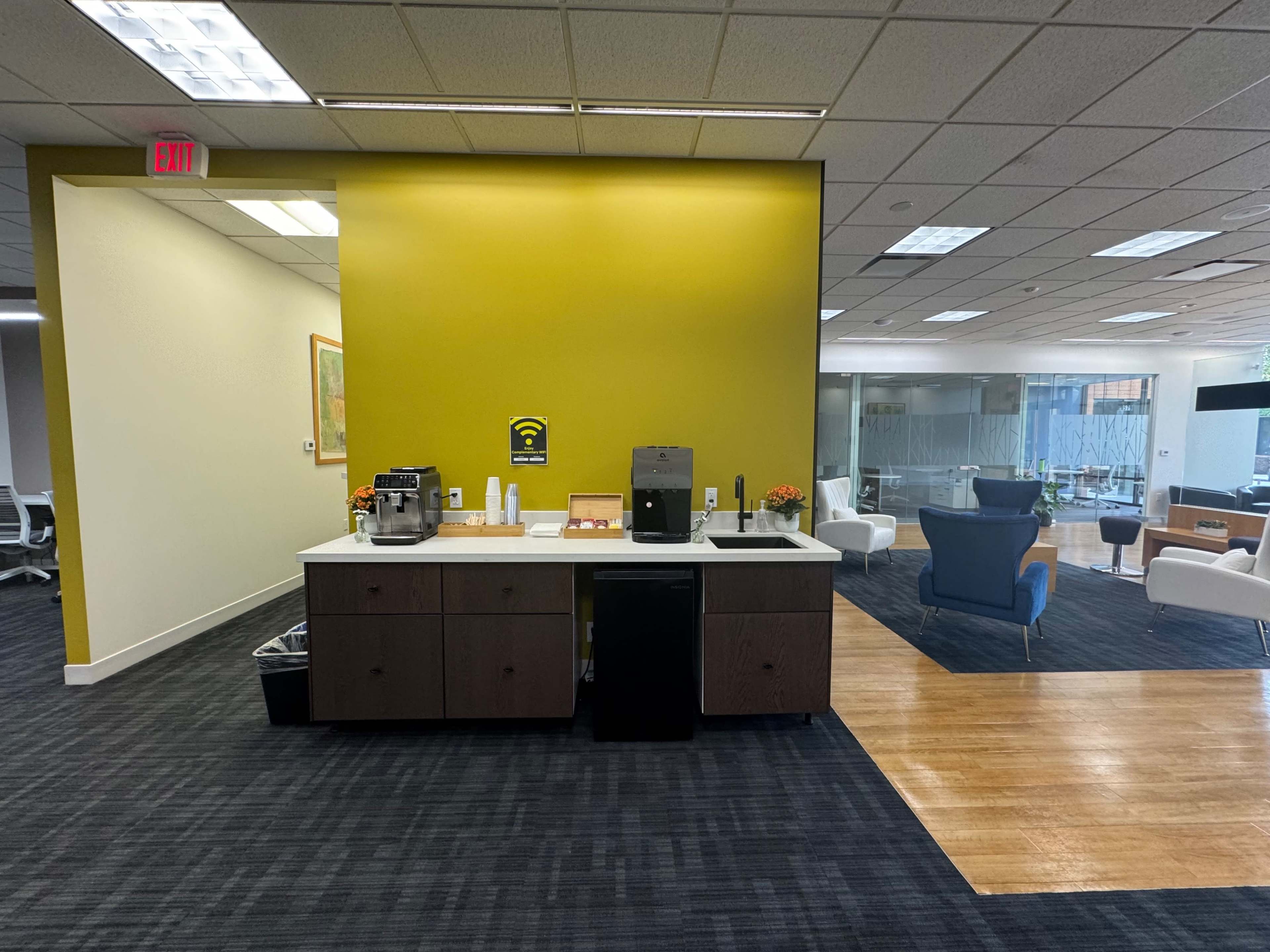 A break area in an office with a coffee station, a small fridge, and seating visible in the background.