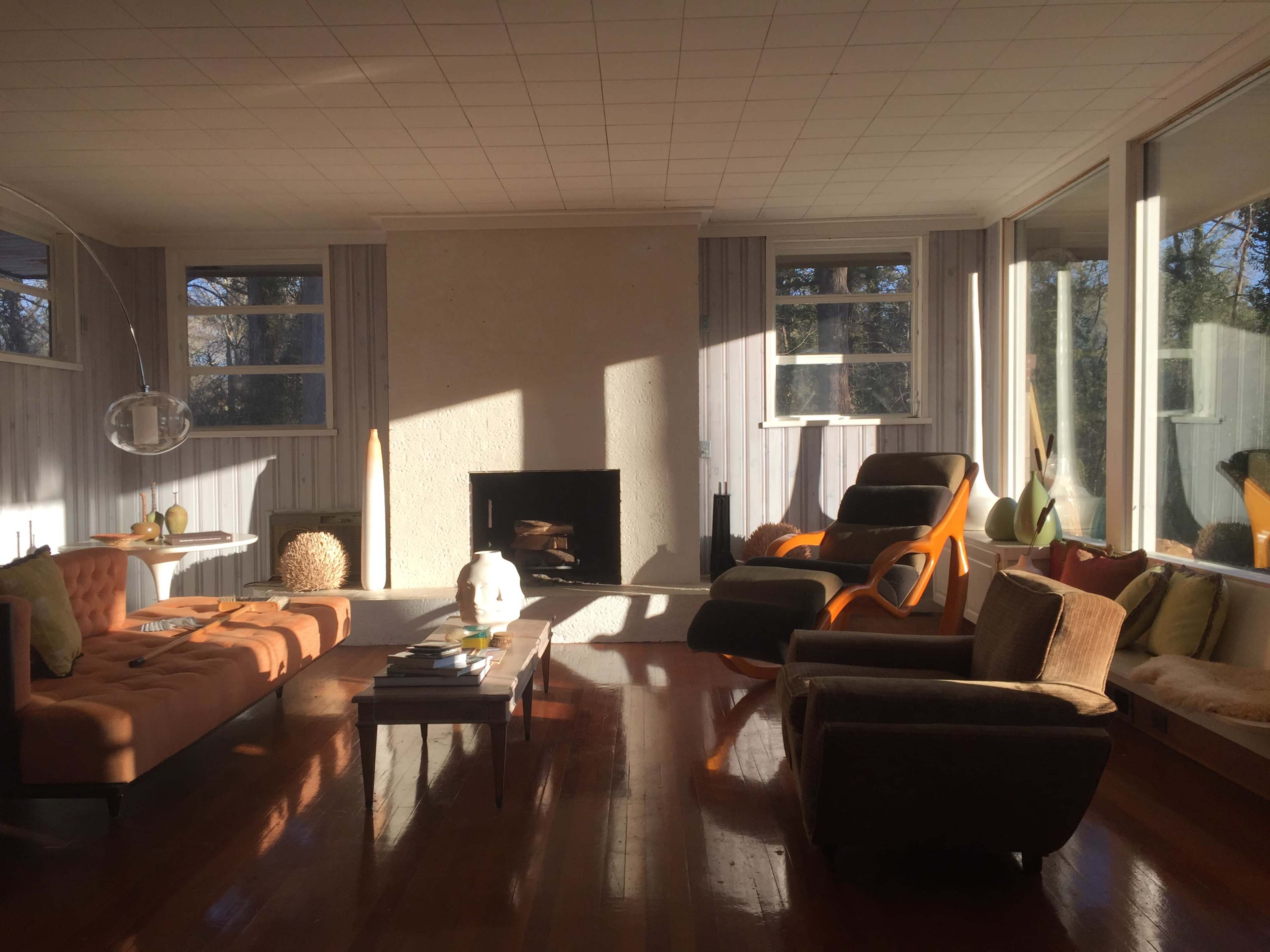 A living room with large windows, a fireplace, and various seating options arranged around a wooden coffee table.
