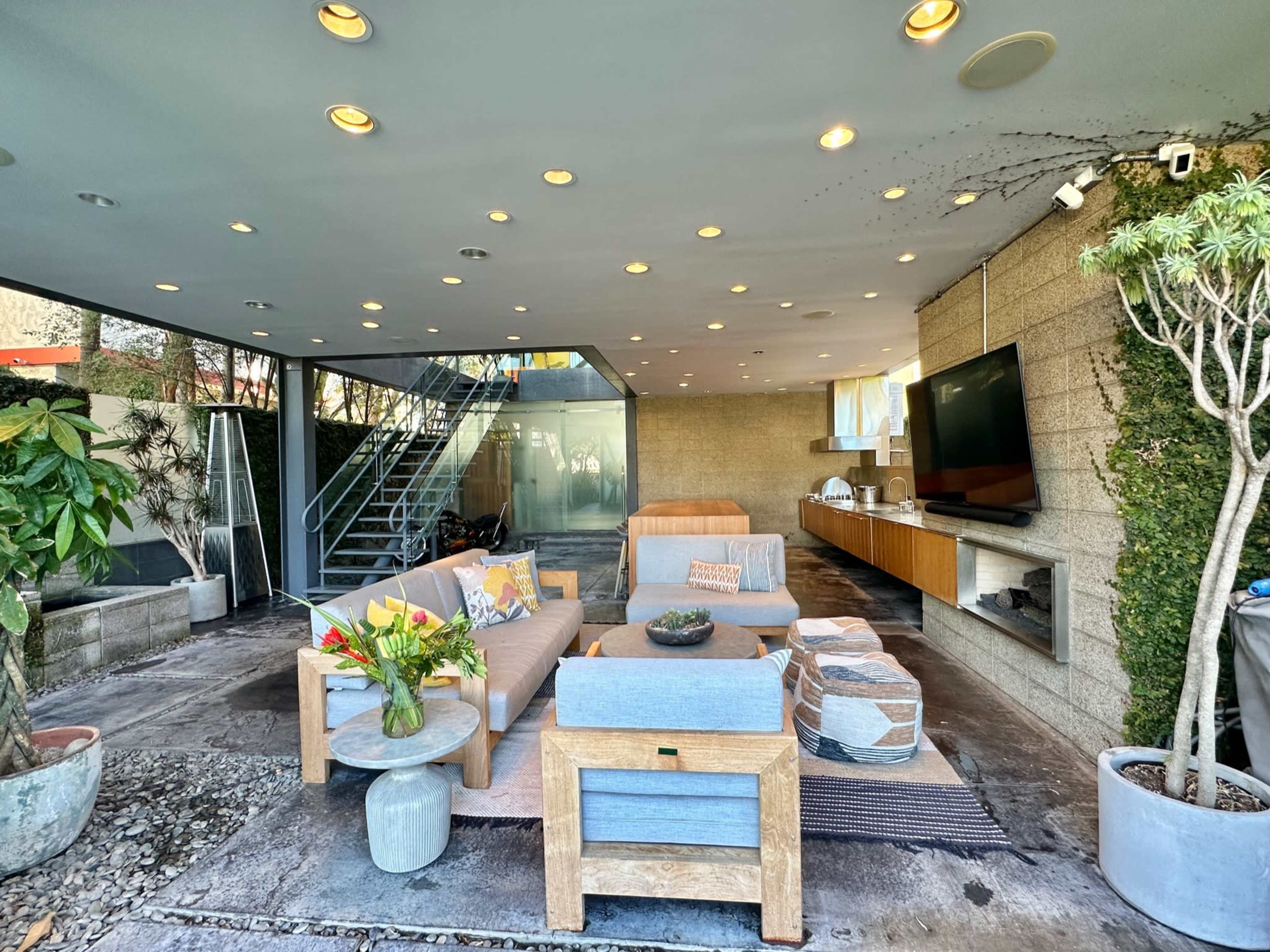 A modern outdoor living space featuring comfortable seating arrangements, decorative plants, and a staircase leading to an upper level.