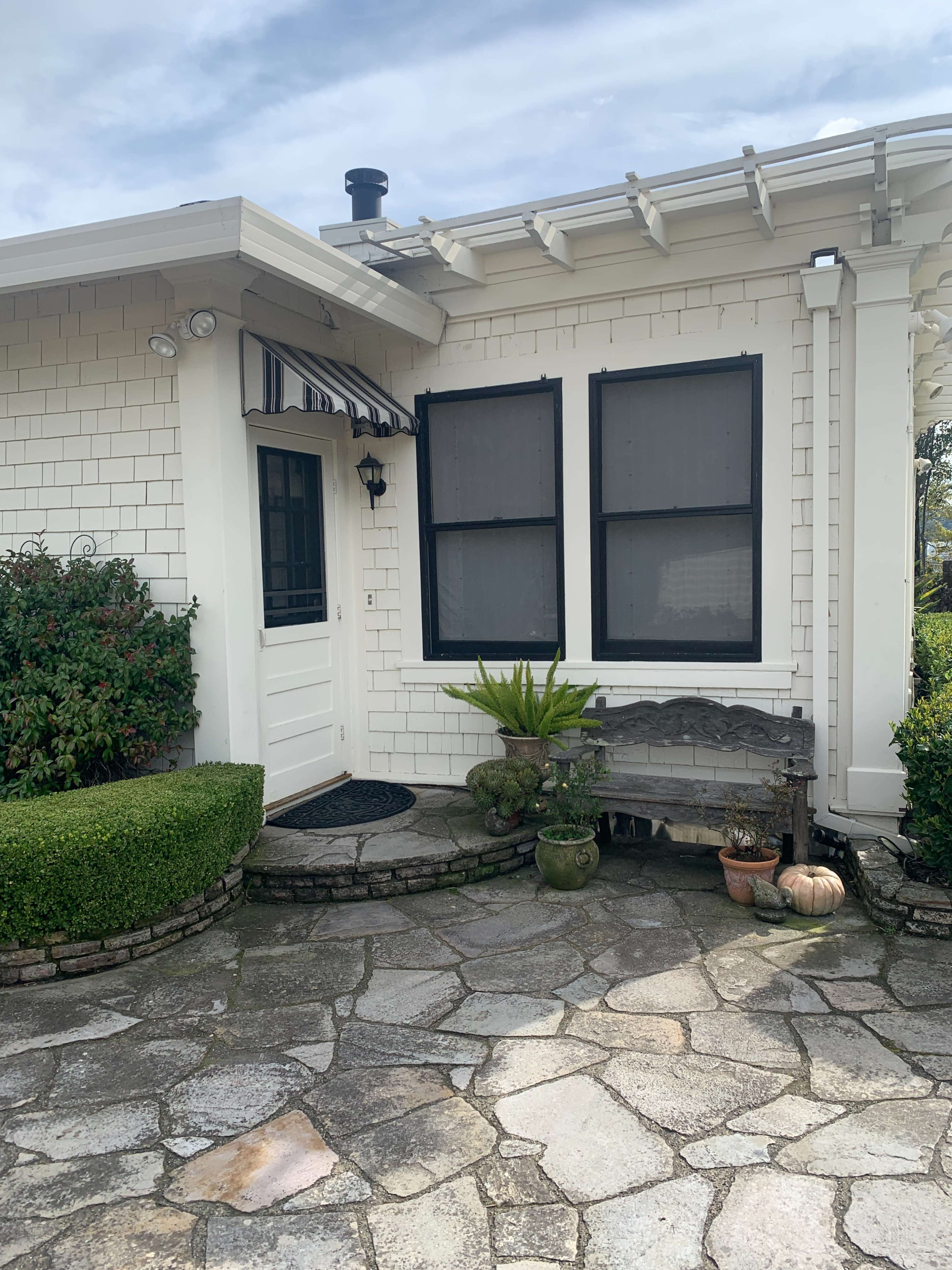 The entrance of a house with a stone pathway, a small garden, and a bench beside potted plants.