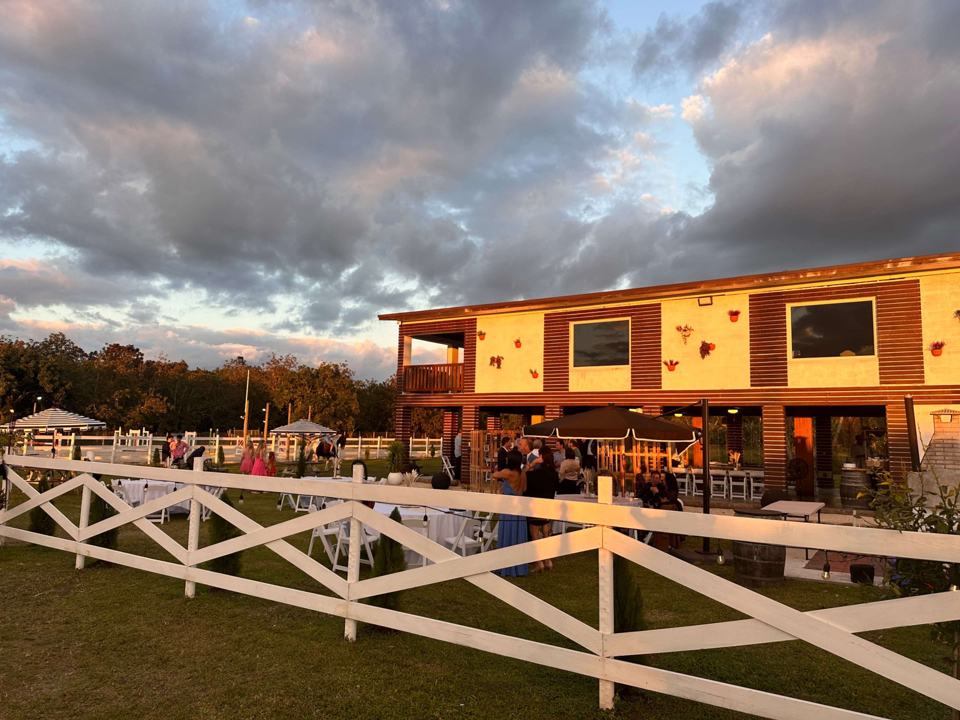 A large wooden building with decorative butterflies and people gathered outside is set against a backdrop of cloudy skies during sunset.