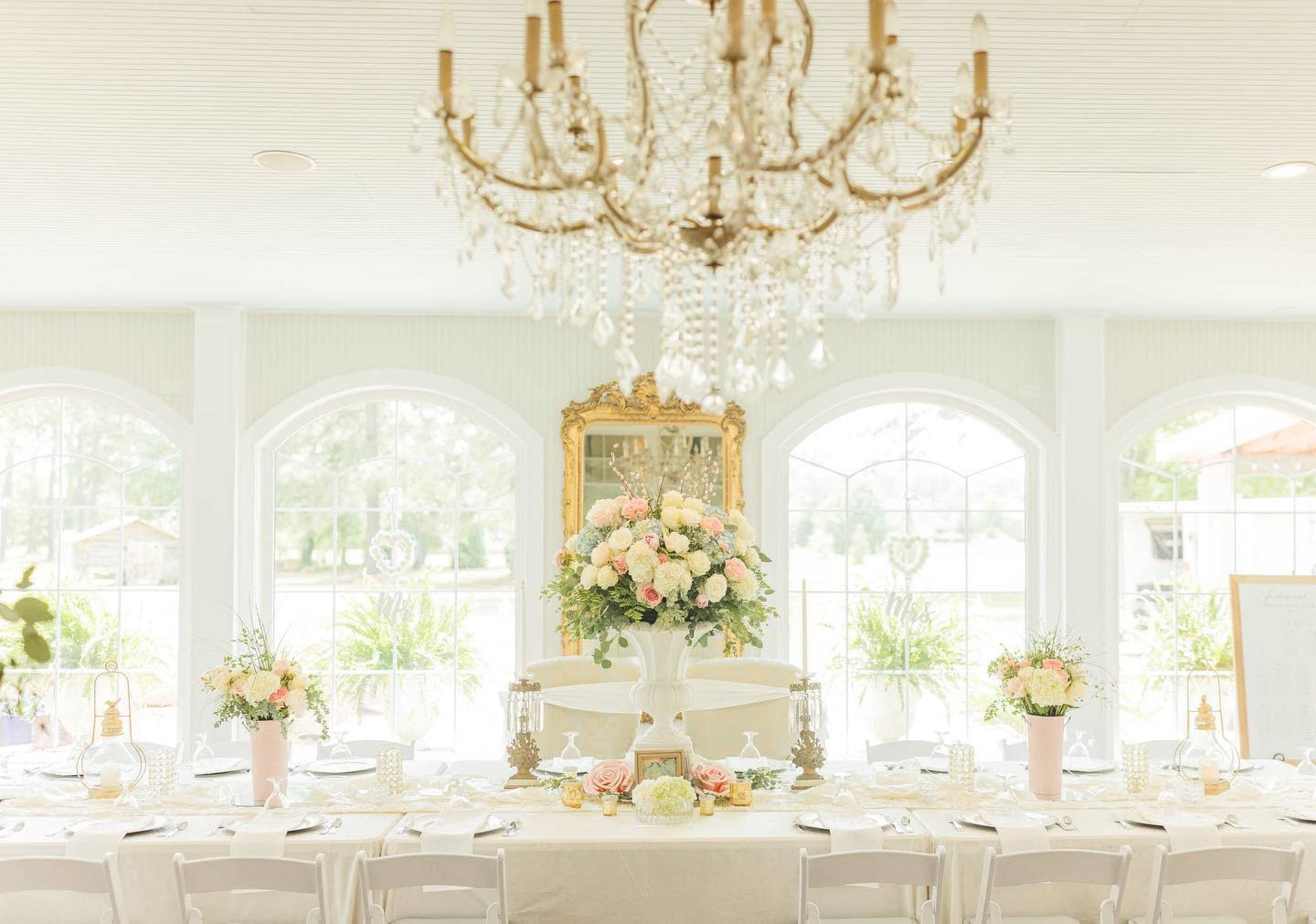 A spacious dining area features a long table set with decorative floral arrangements, elegant tableware, and a large chandelier overhead.