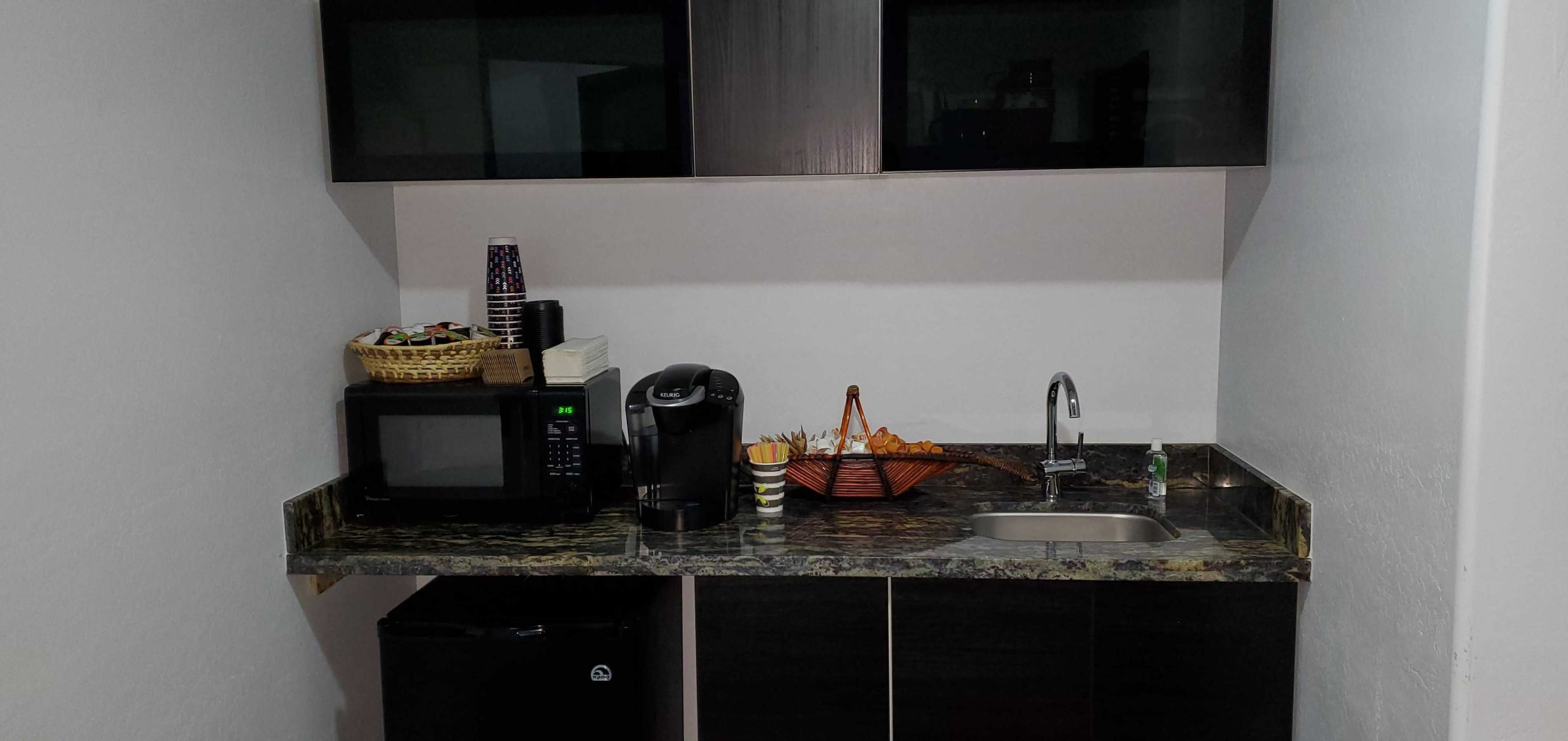 A kitchen corner with a microwave, coffee maker, sink, and a basket of snacks on a countertop.