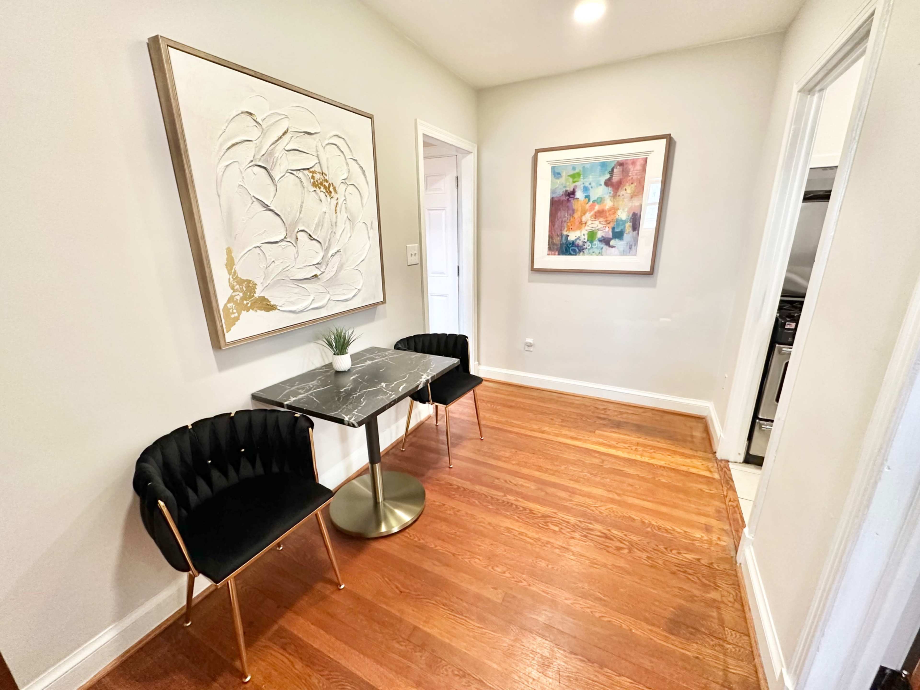 A small seating area with two black chairs and a round marble-top table flanked by wall art on a hardwood floor.