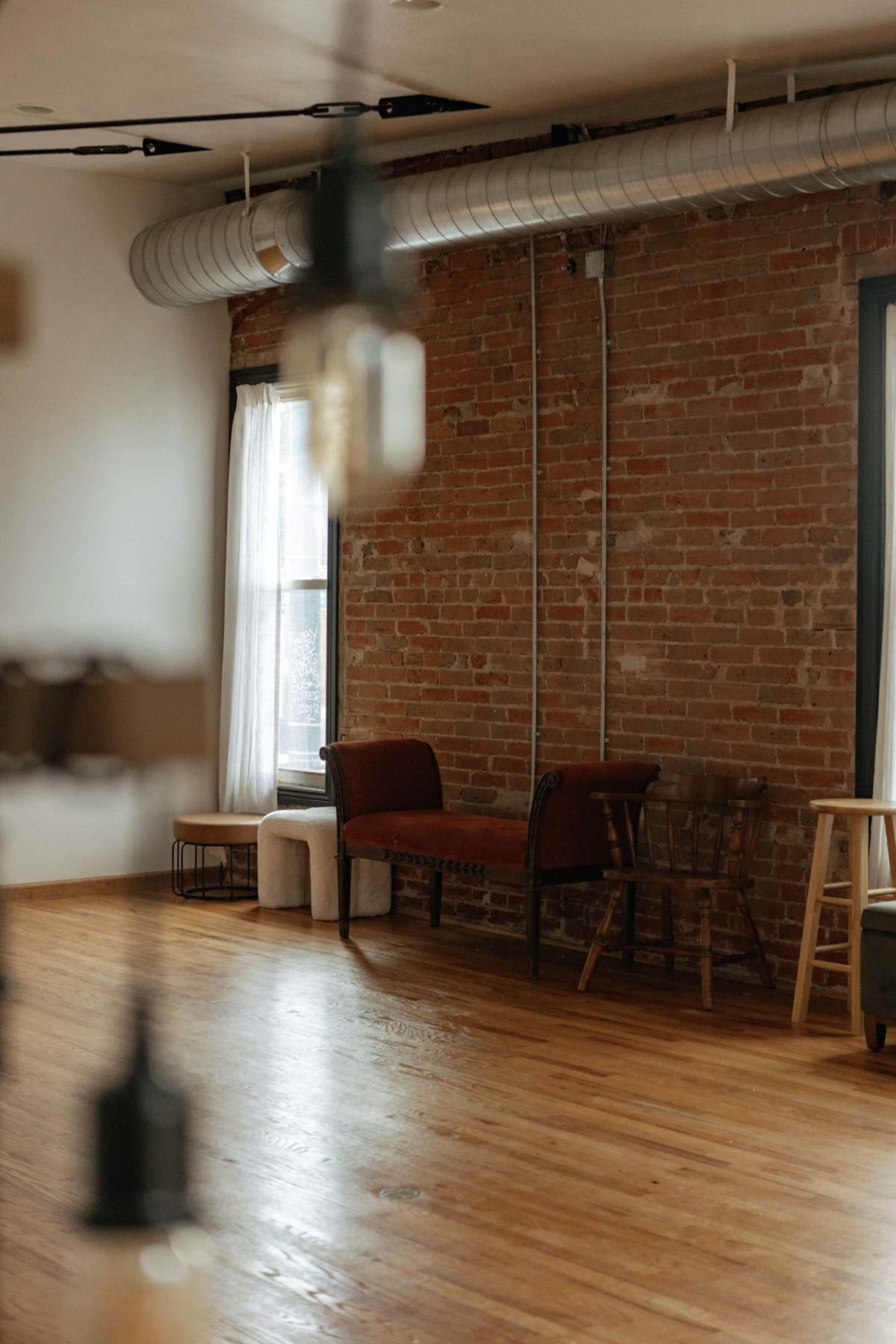 The image shows an interior space with exposed brick walls, wooden floors, and a mix of seating options in a well-lit area.