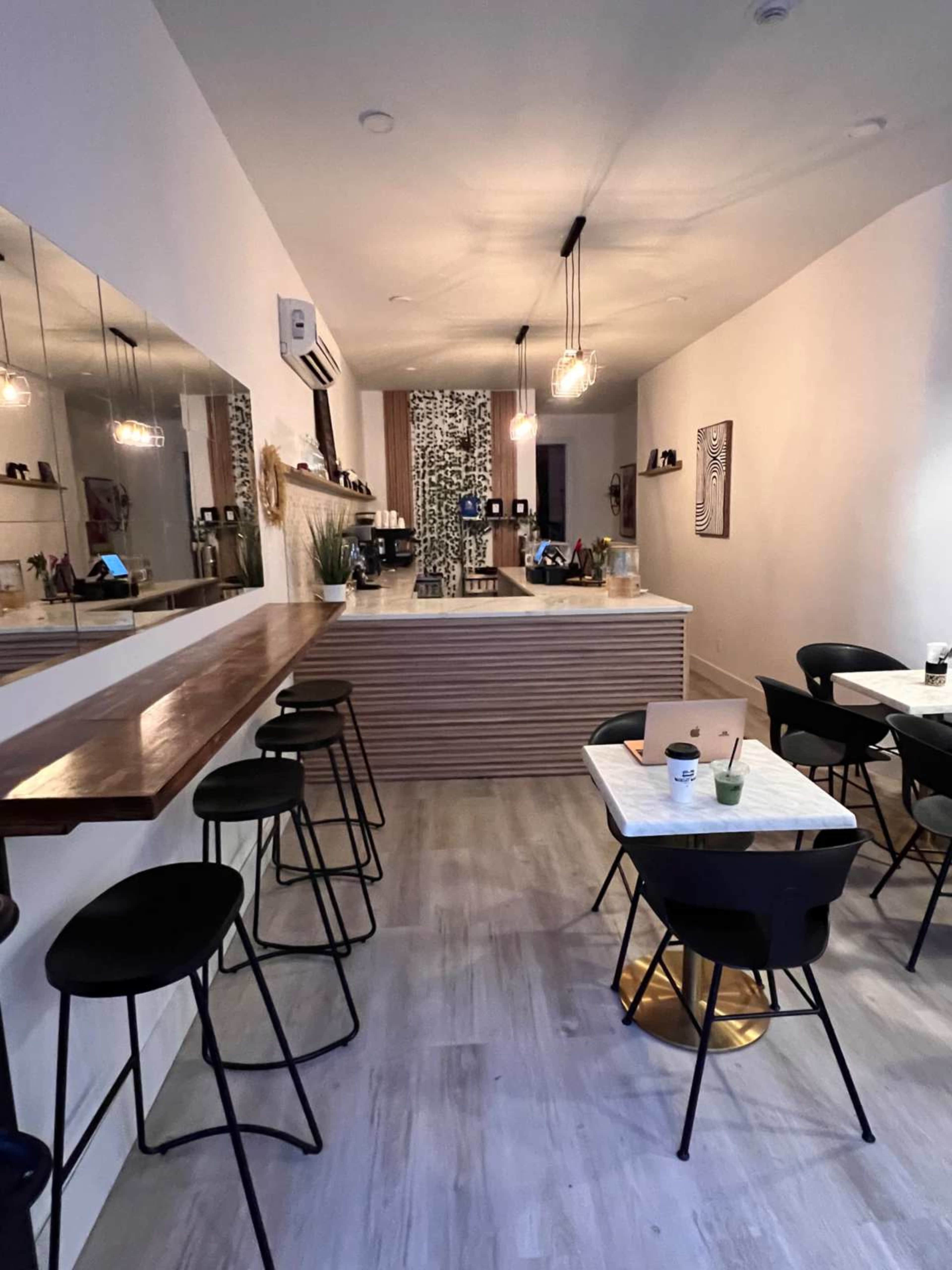 The image shows a modern café interior with a bar area, several black stools, a marble table, and a patterned wall behind the counter.