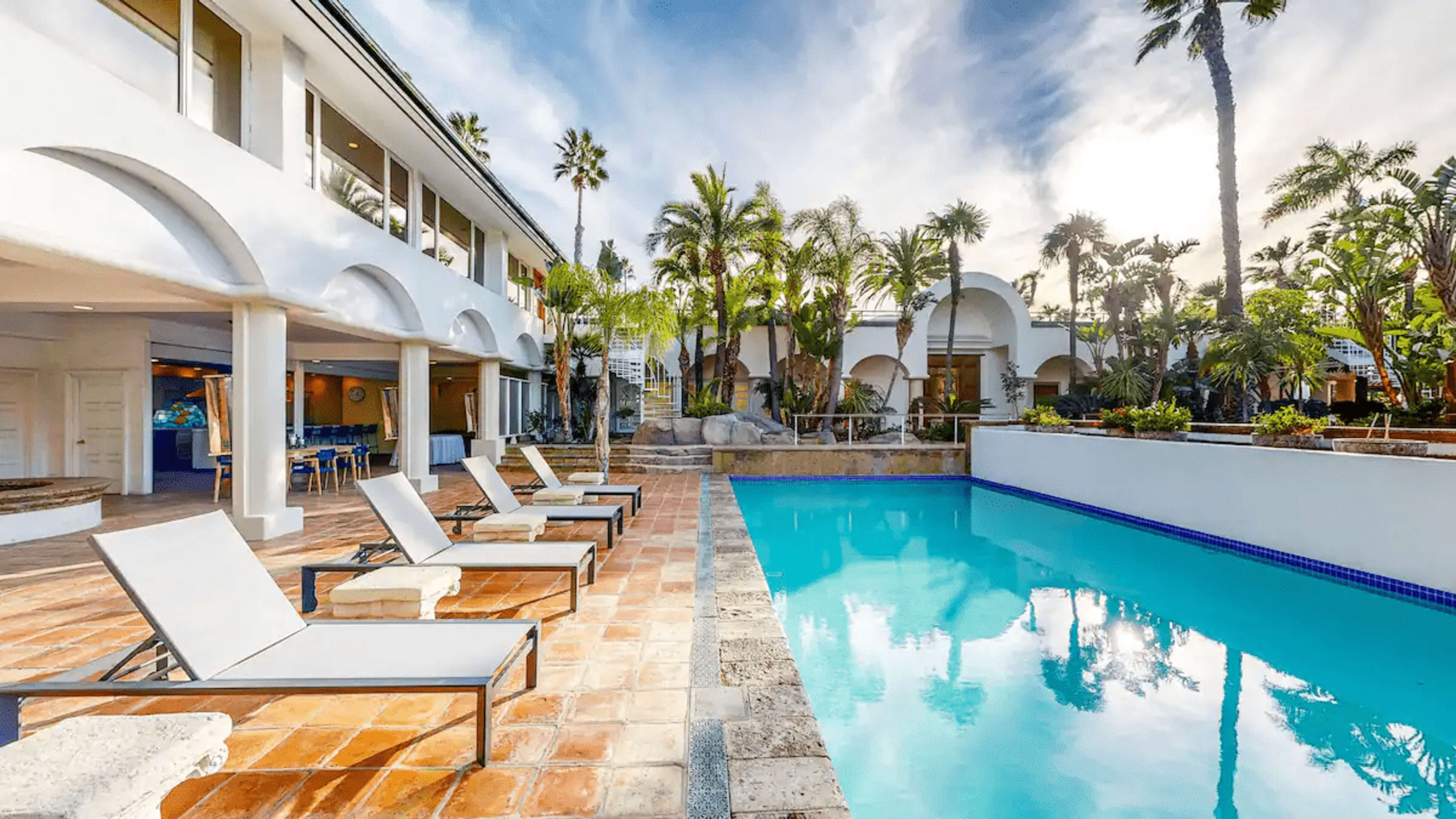 A landscaped swimming pool area with lounge chairs and palm trees, adjacent to a modern two-story building.