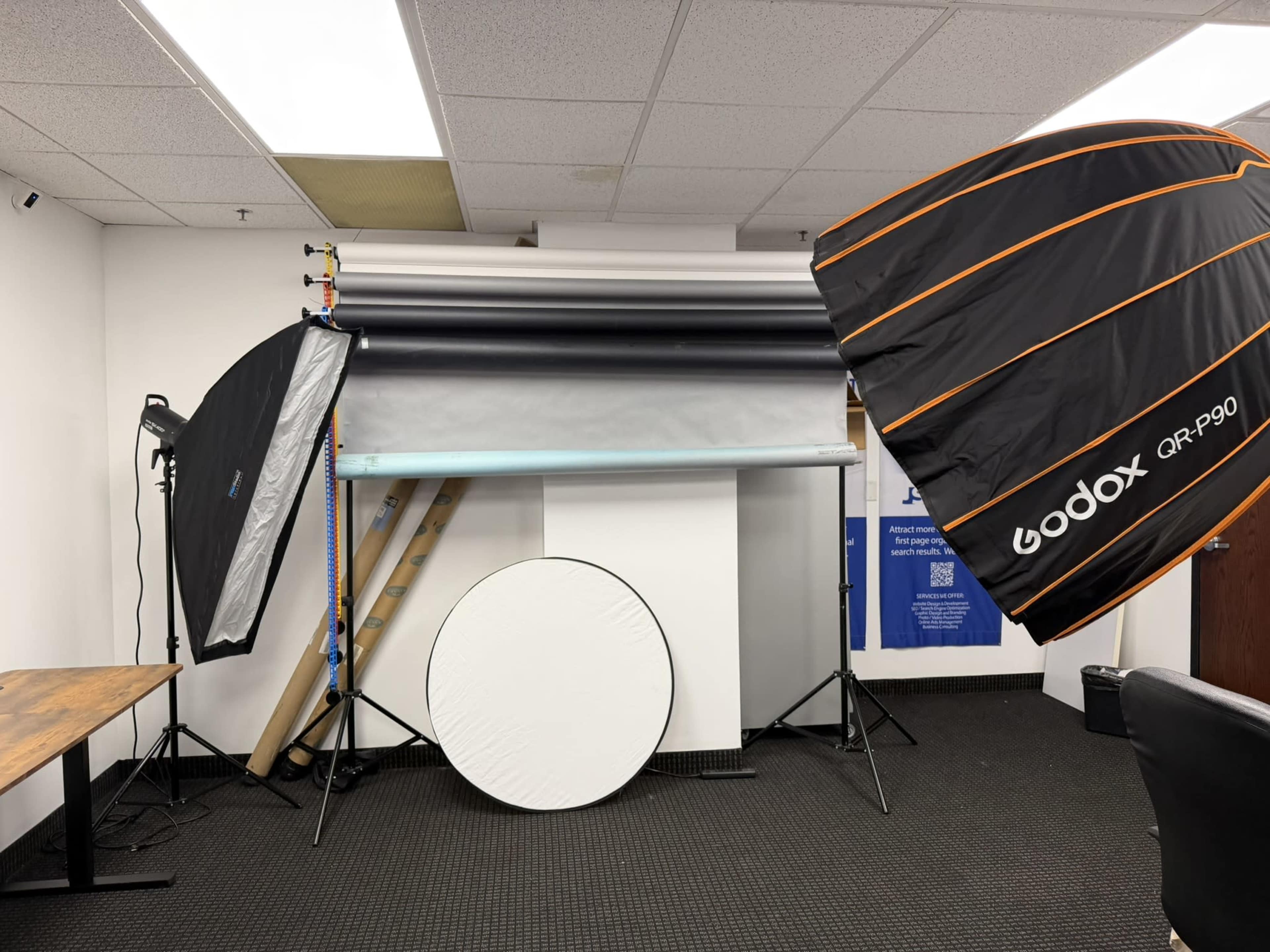 The image shows a photography studio setup featuring a backdrop, a softbox light, a round reflector, and additional lighting equipment.