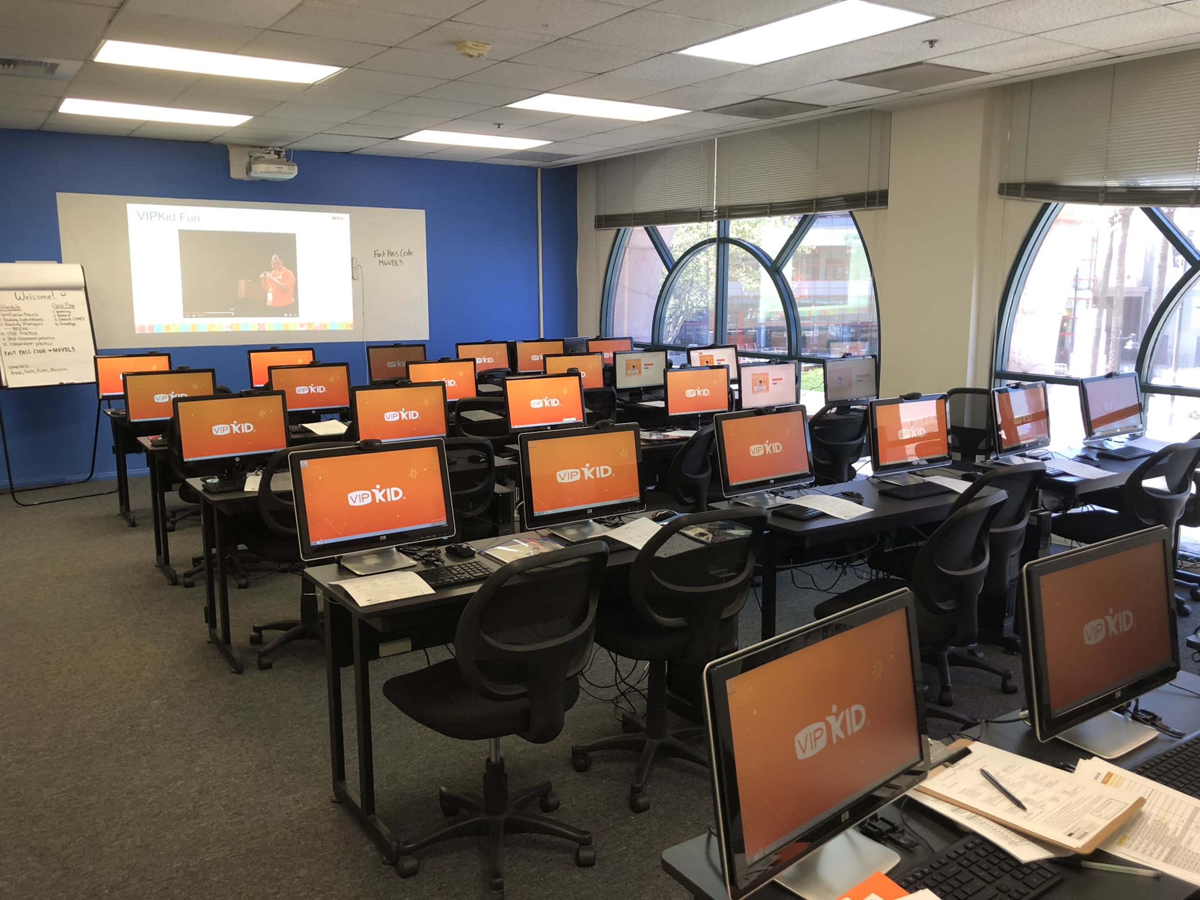 A classroom filled with multiple desktop computers arranged in rows, featuring a presentation on a screen at the front.
