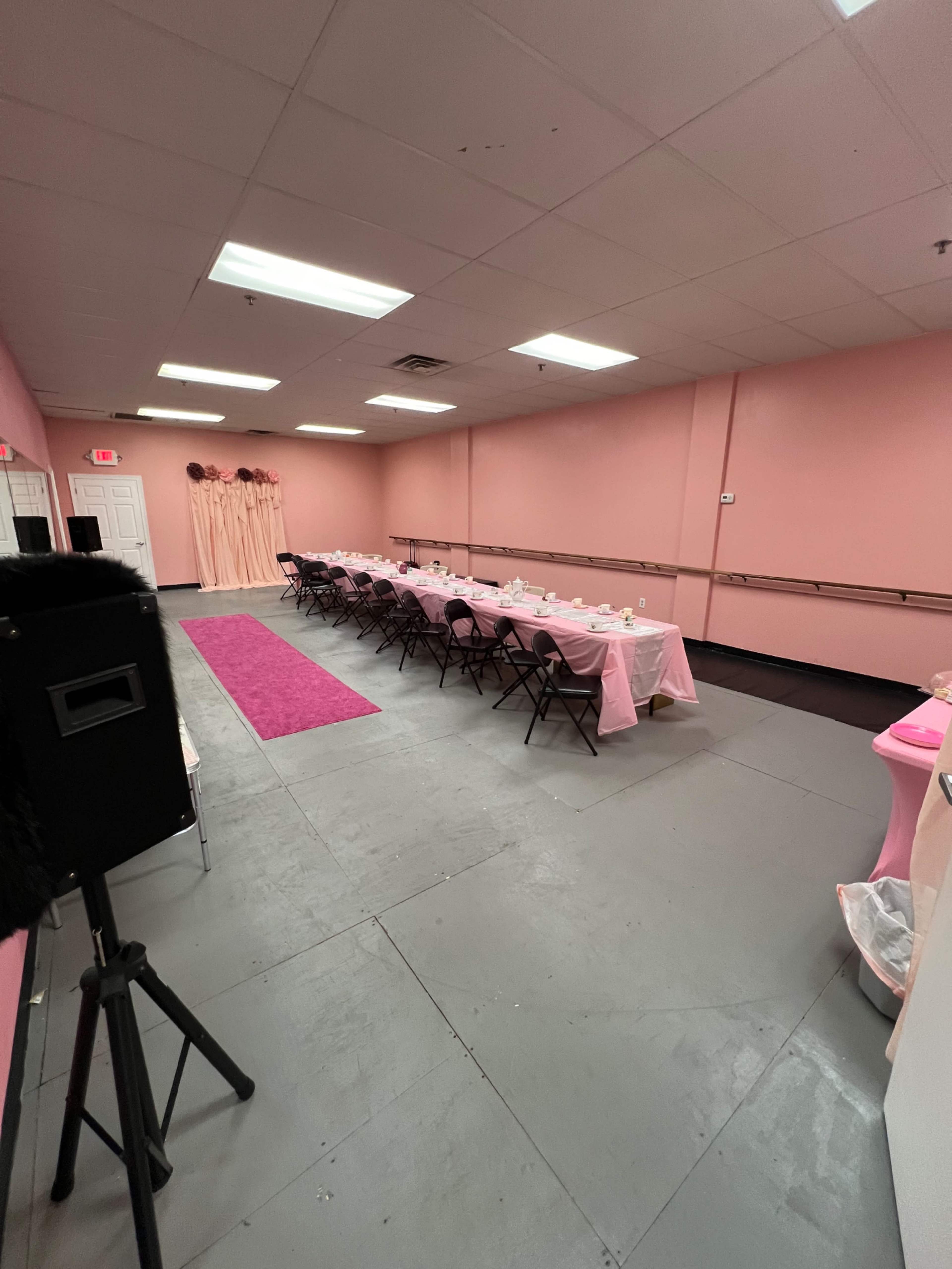 A room with pink walls and a long table set with pink tablecloths and chairs, arranged for an event.