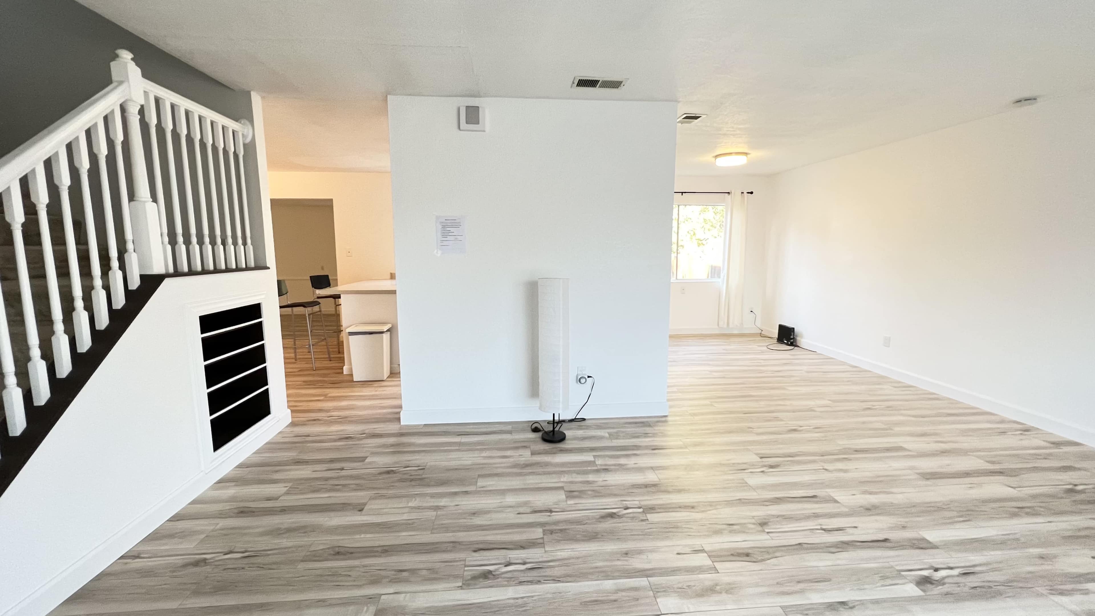 The image shows a spacious living area with a staircase on the left and a large window allowing natural light to enter.