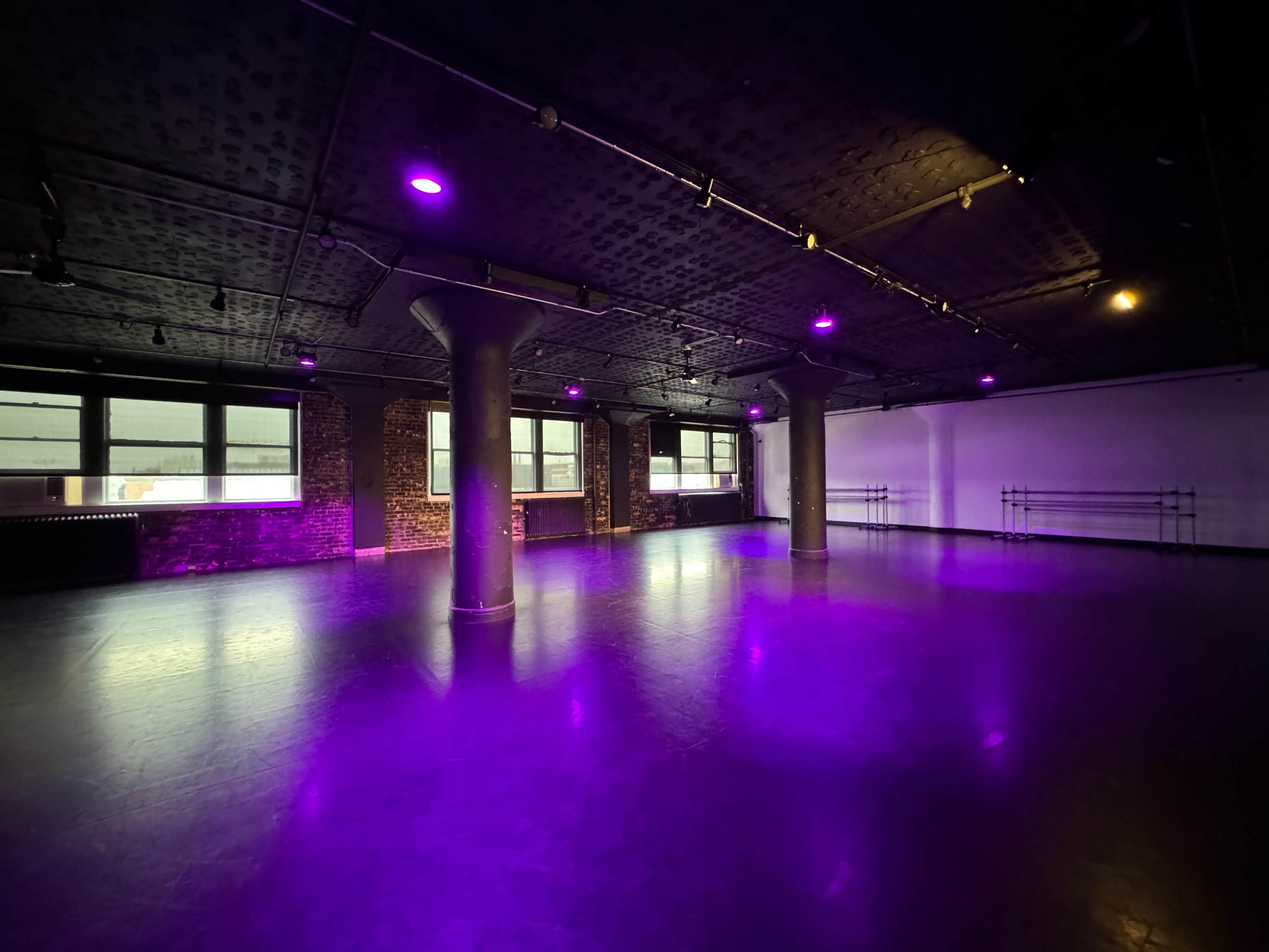 An empty studio space with purple lighting, exposed brick walls, and pillars in a large room.