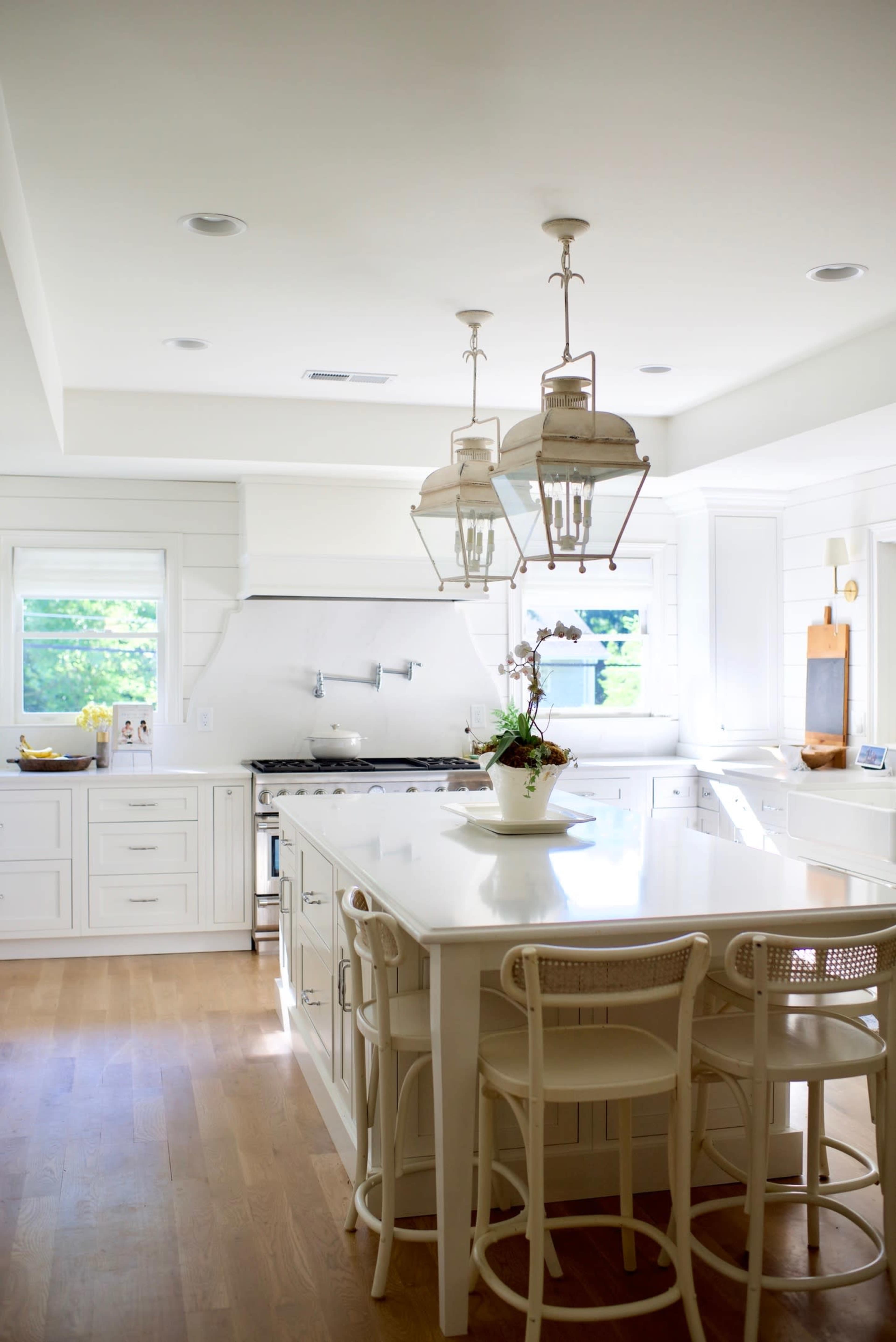 A modern kitchen features white cabinetry, a large island with bar stools, and pendant lighting above.