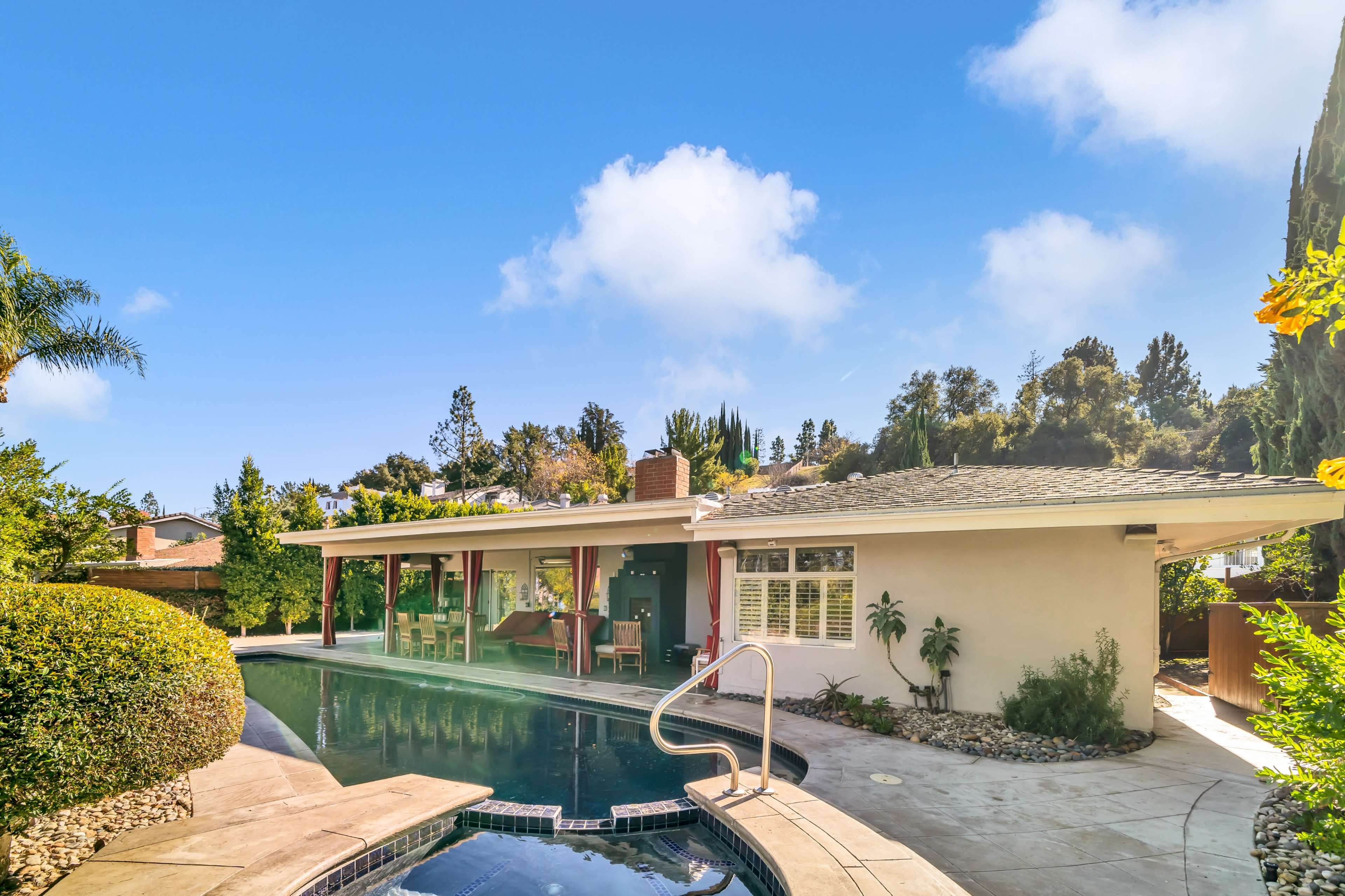 The image shows a modern house with a swimming pool surrounded by greenery and a clear blue sky.