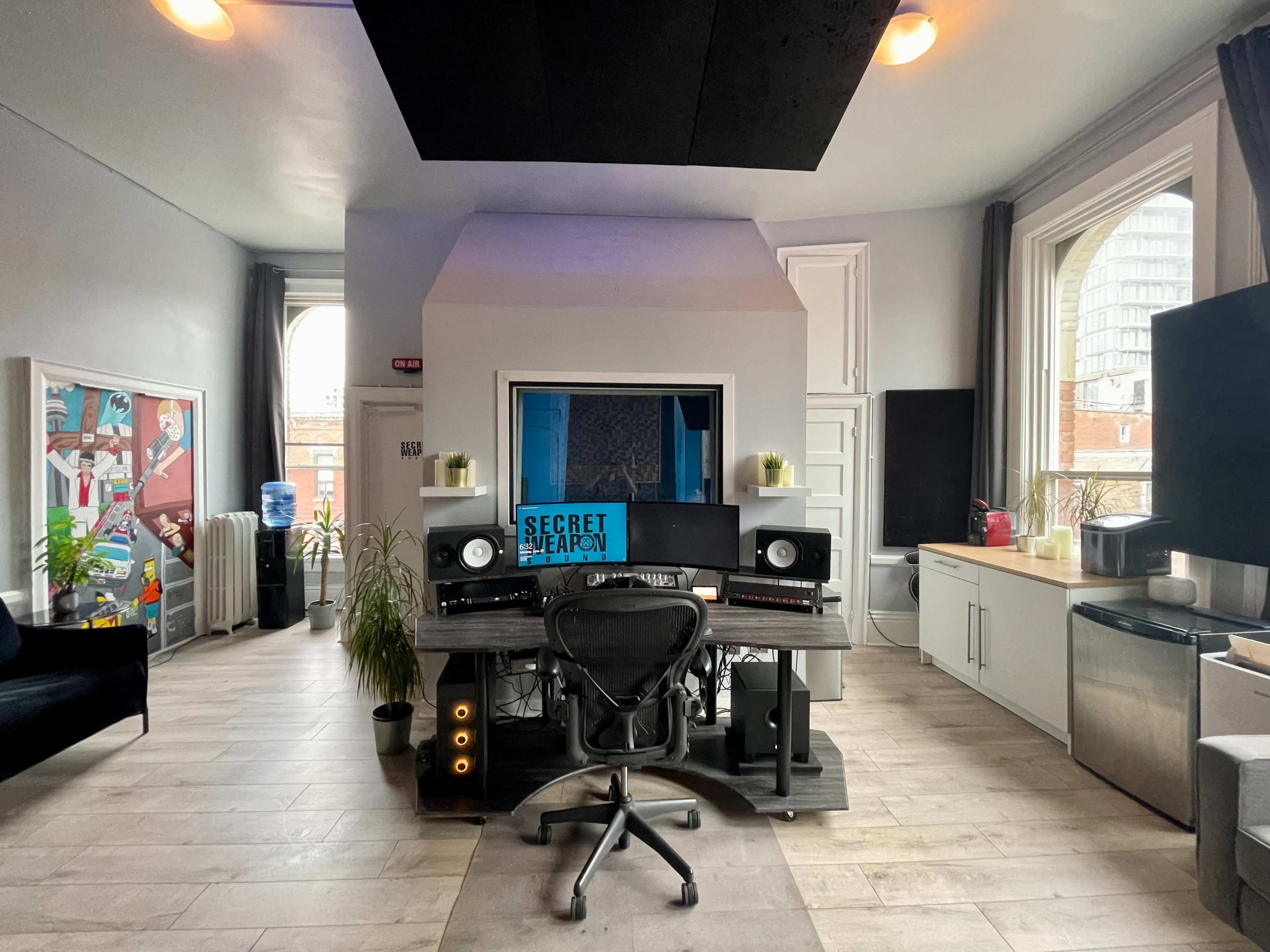 A modern music studio with a central workstation, large windows, and various audio equipment arranged on a sleek desk.