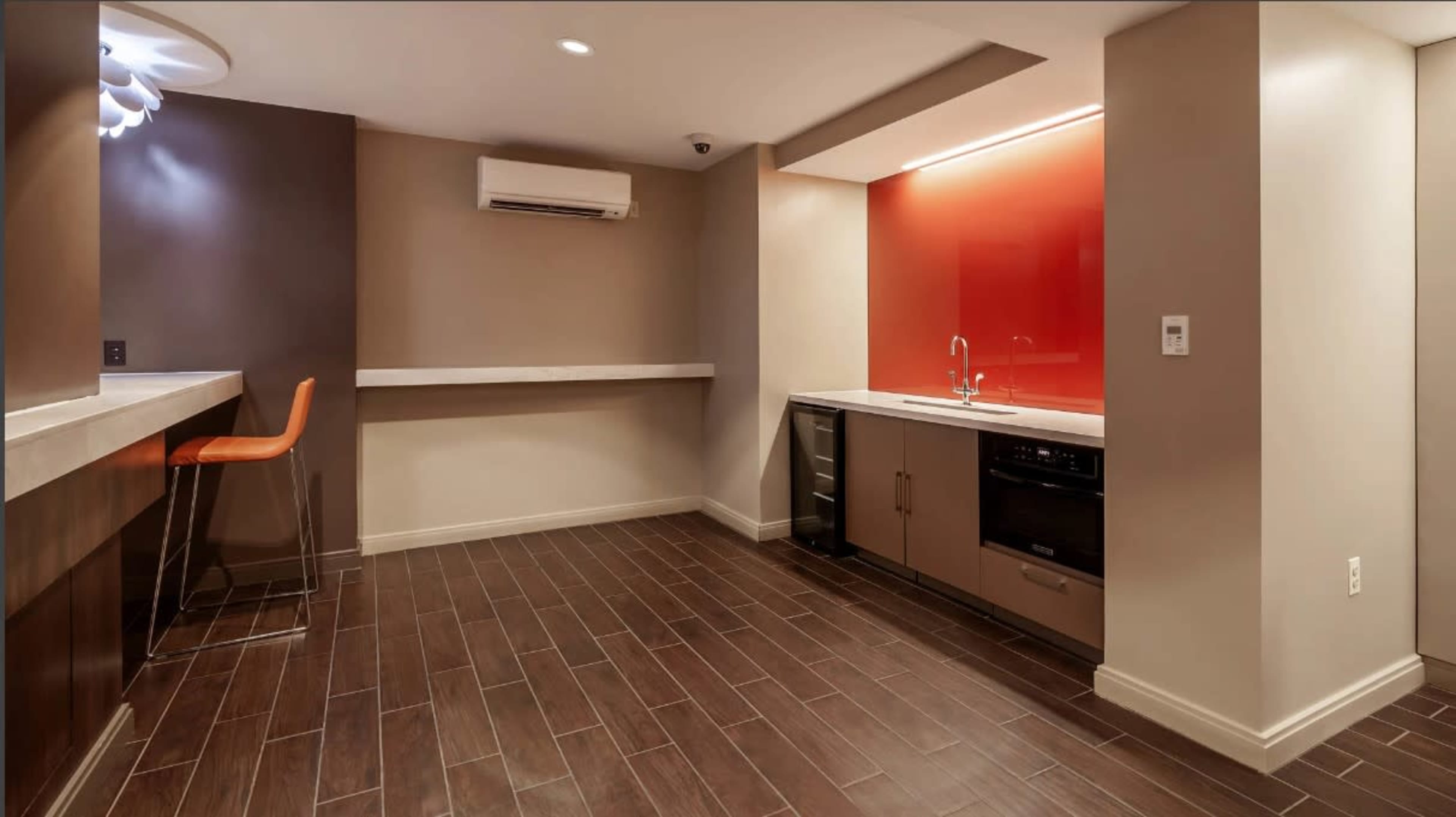 A modern kitchenette area with a bar counter, an orange accent wall, and kitchen appliances including a sink and a refrigerator.