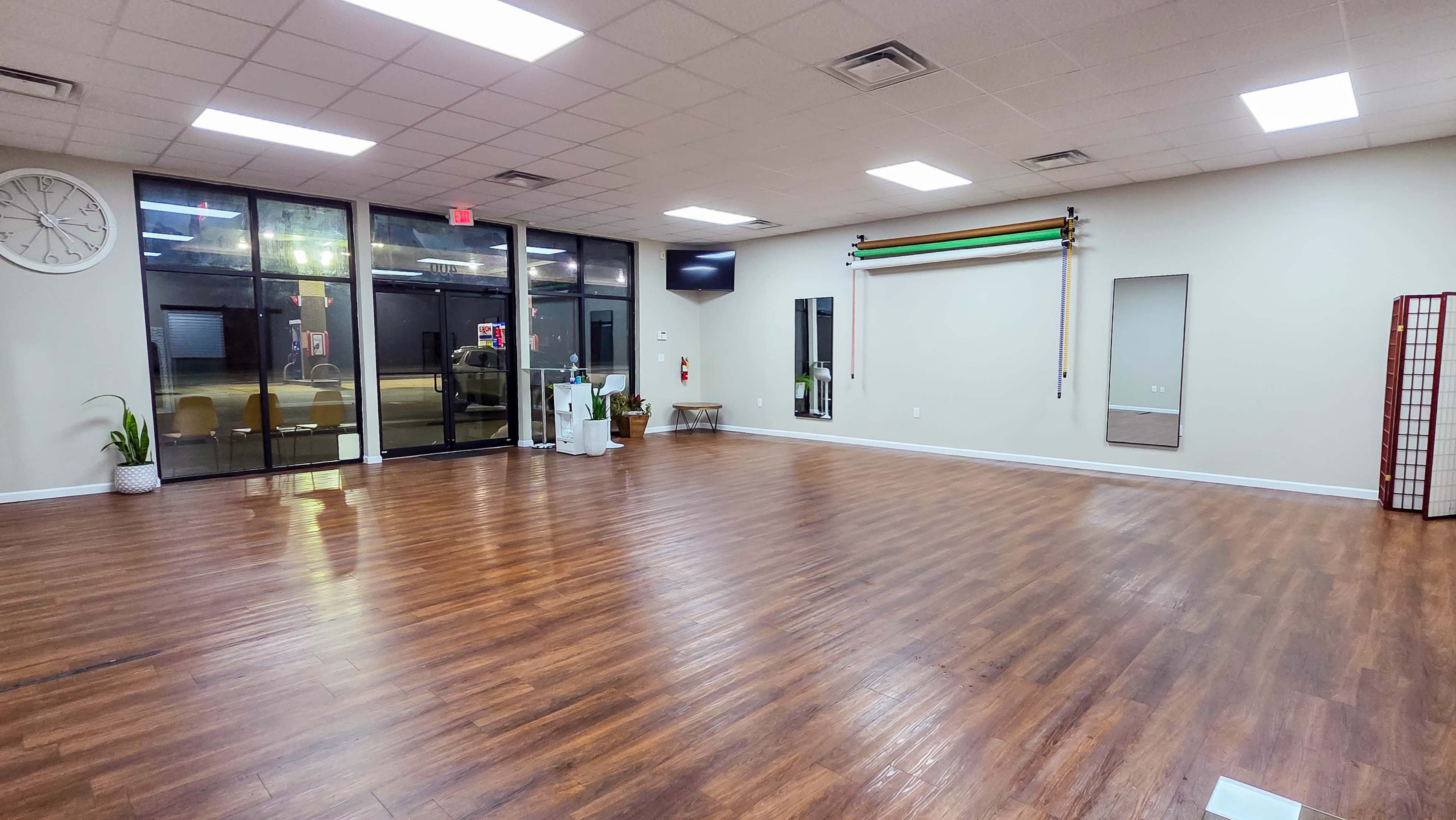 The image shows a large, empty studio space with wooden flooring, large windows, and minimal furnishings.
