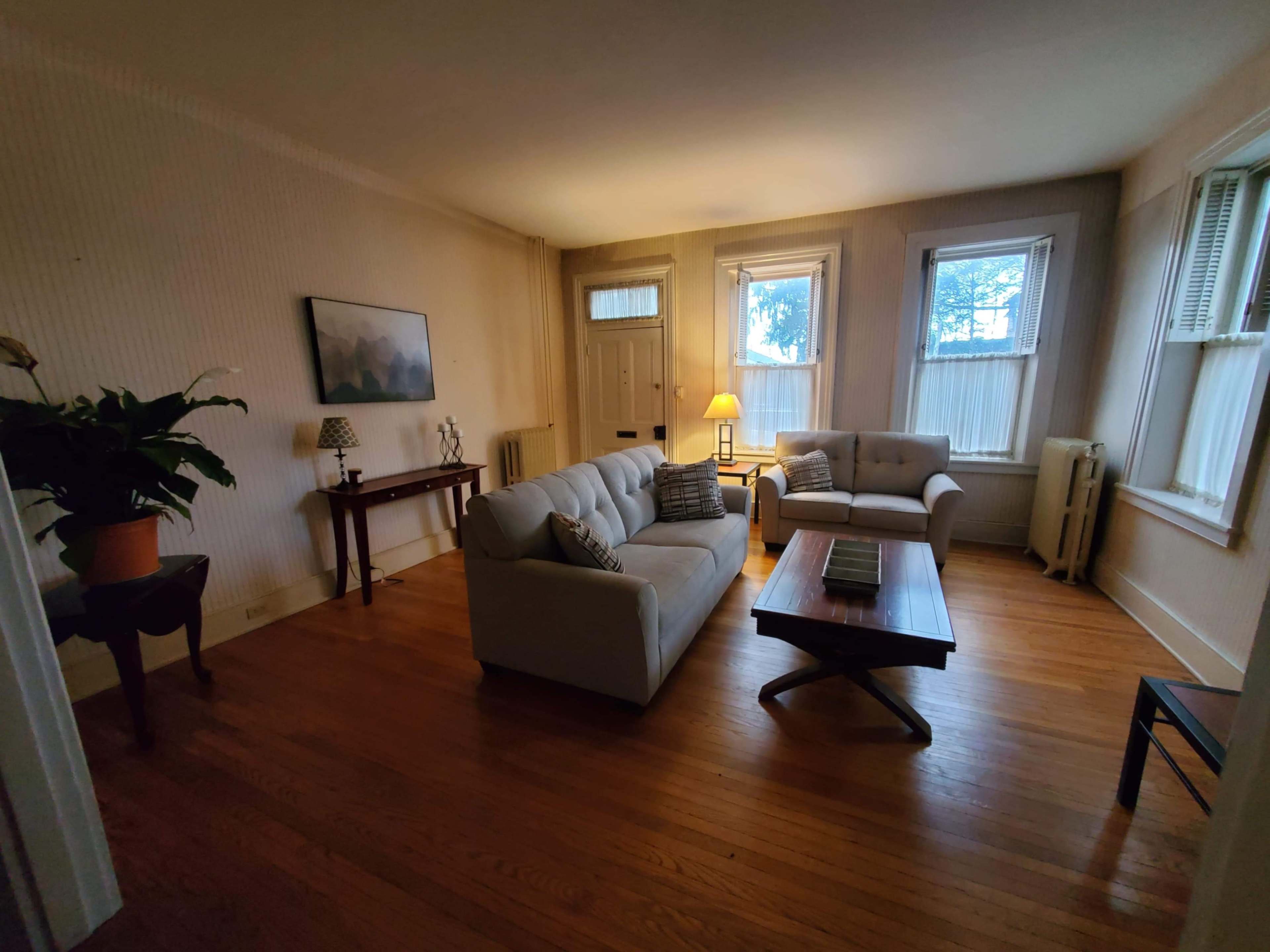 A living room with a light-colored couch, a coffee table, a side table with a lamp, and windows allowing natural light.