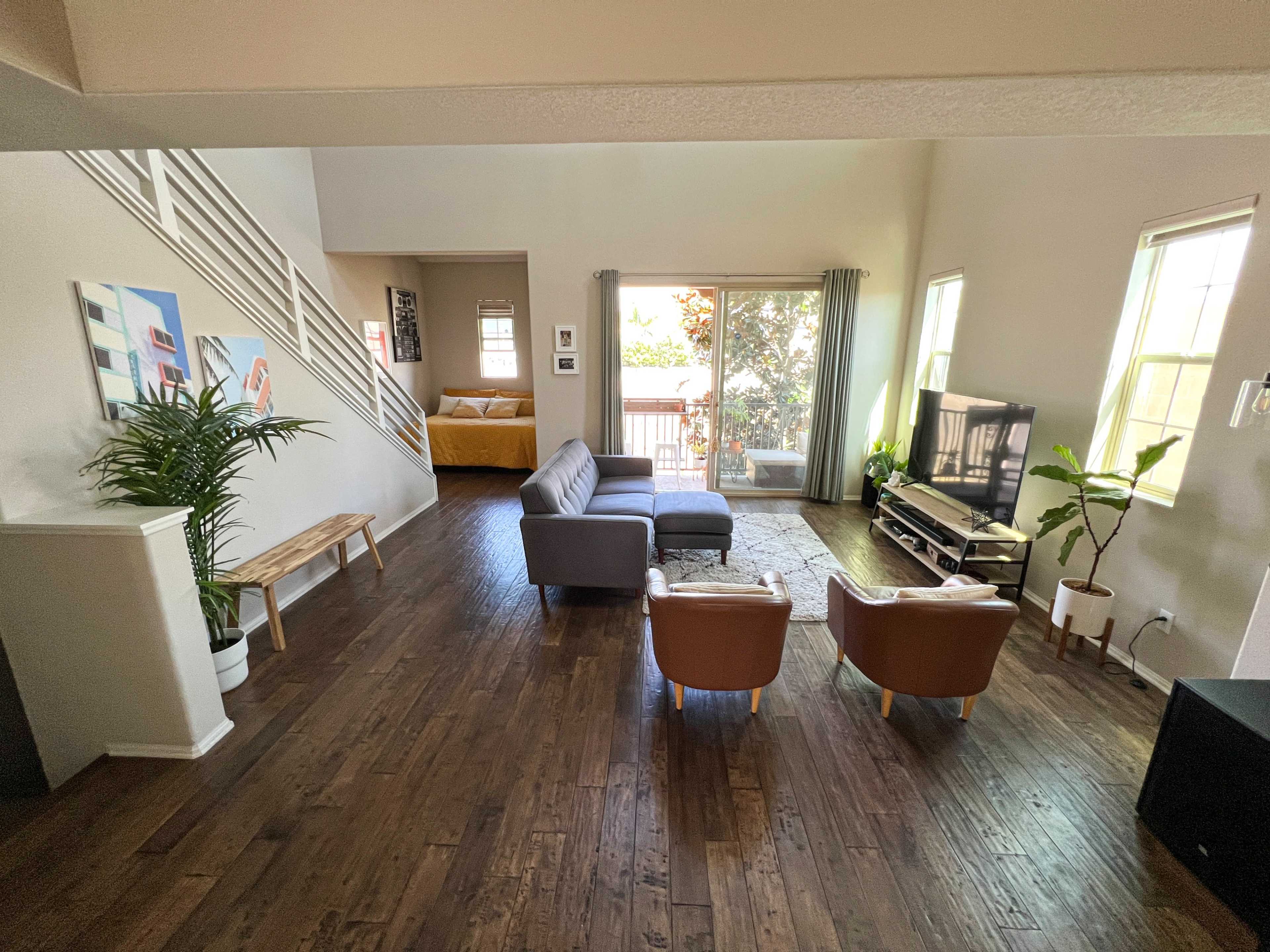 A spacious living room with a couch, two chairs, a coffee table, and large windows that allow natural light, leading to an outdoor deck.