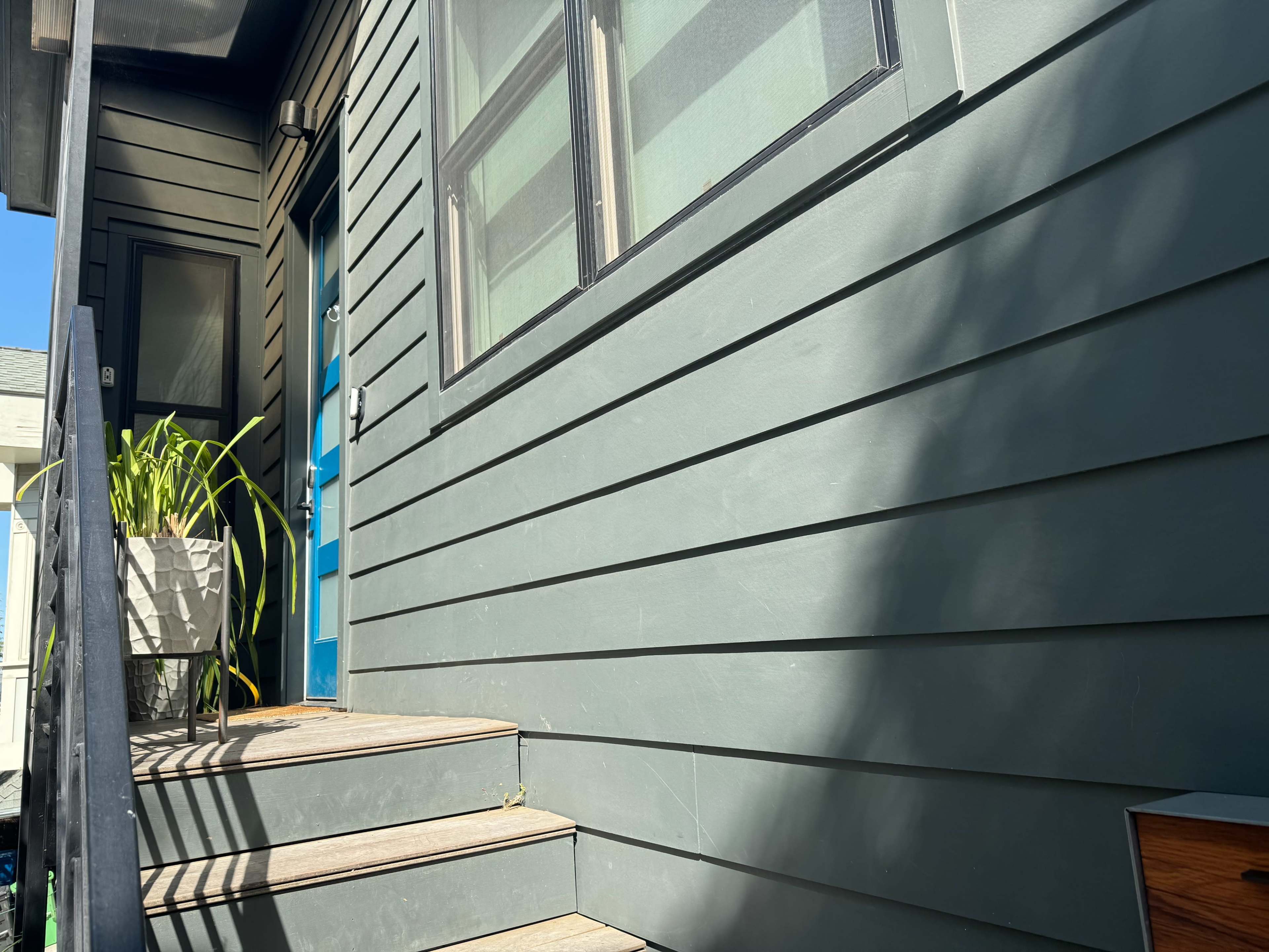 A house with gray siding, a blue front door, and wooden steps leading up to a porch.