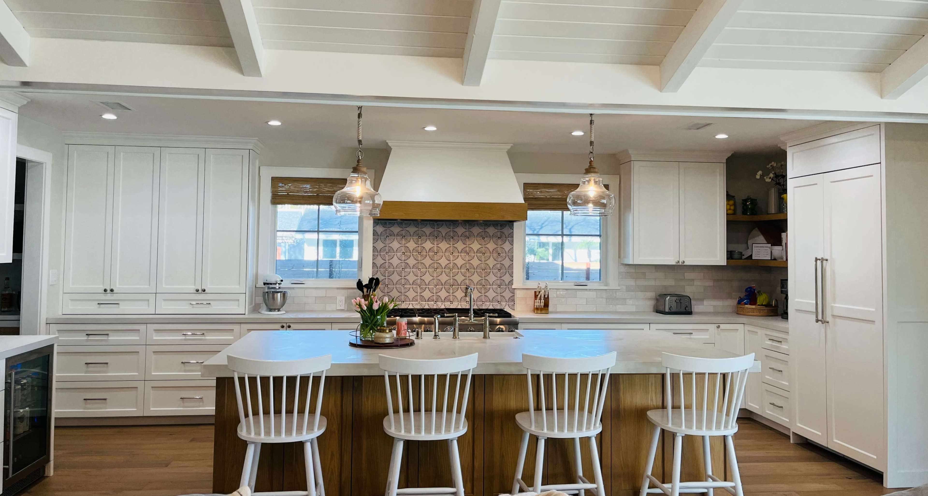 The kitchen features a large central island with seating for four, white cabinets, a patterned backsplash, and modern pendant lighting.