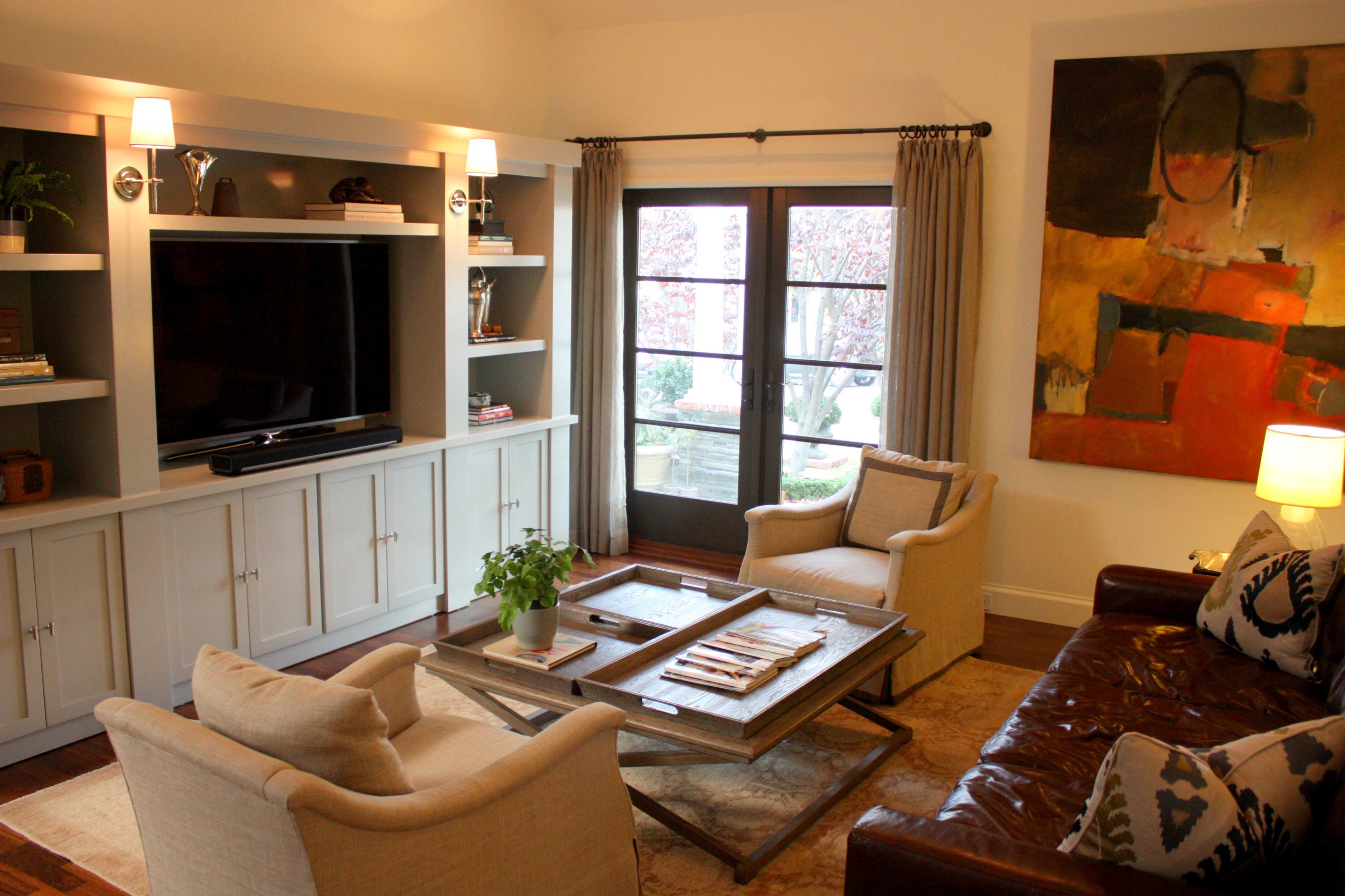 A living room with a television unit, two armchairs, a coffee table, and a large abstract painting on the wall.