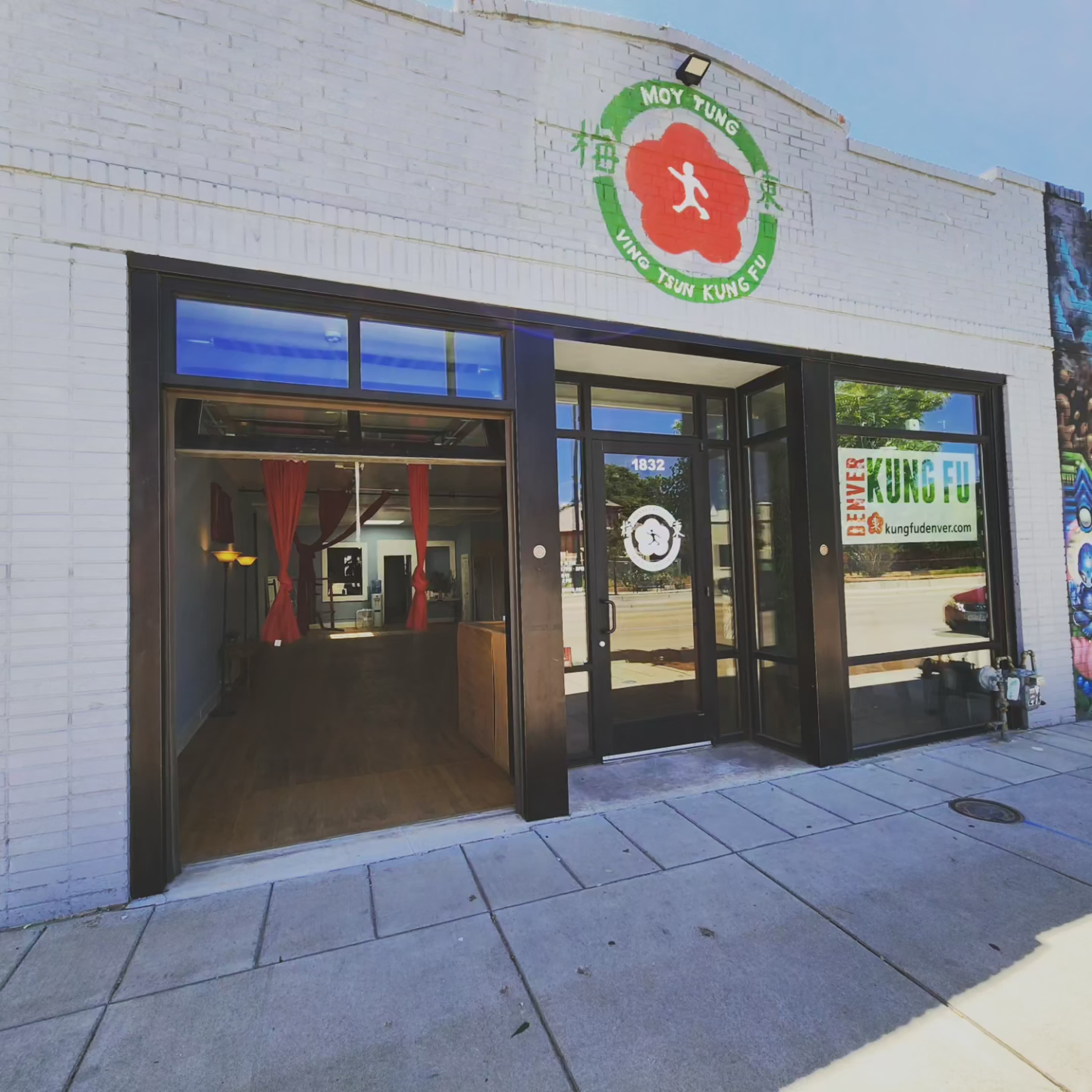 The image shows the entrance of a martial arts studio labeled "Moy Tung Kung Fu," featuring large glass doors and a mural on the exterior wall.