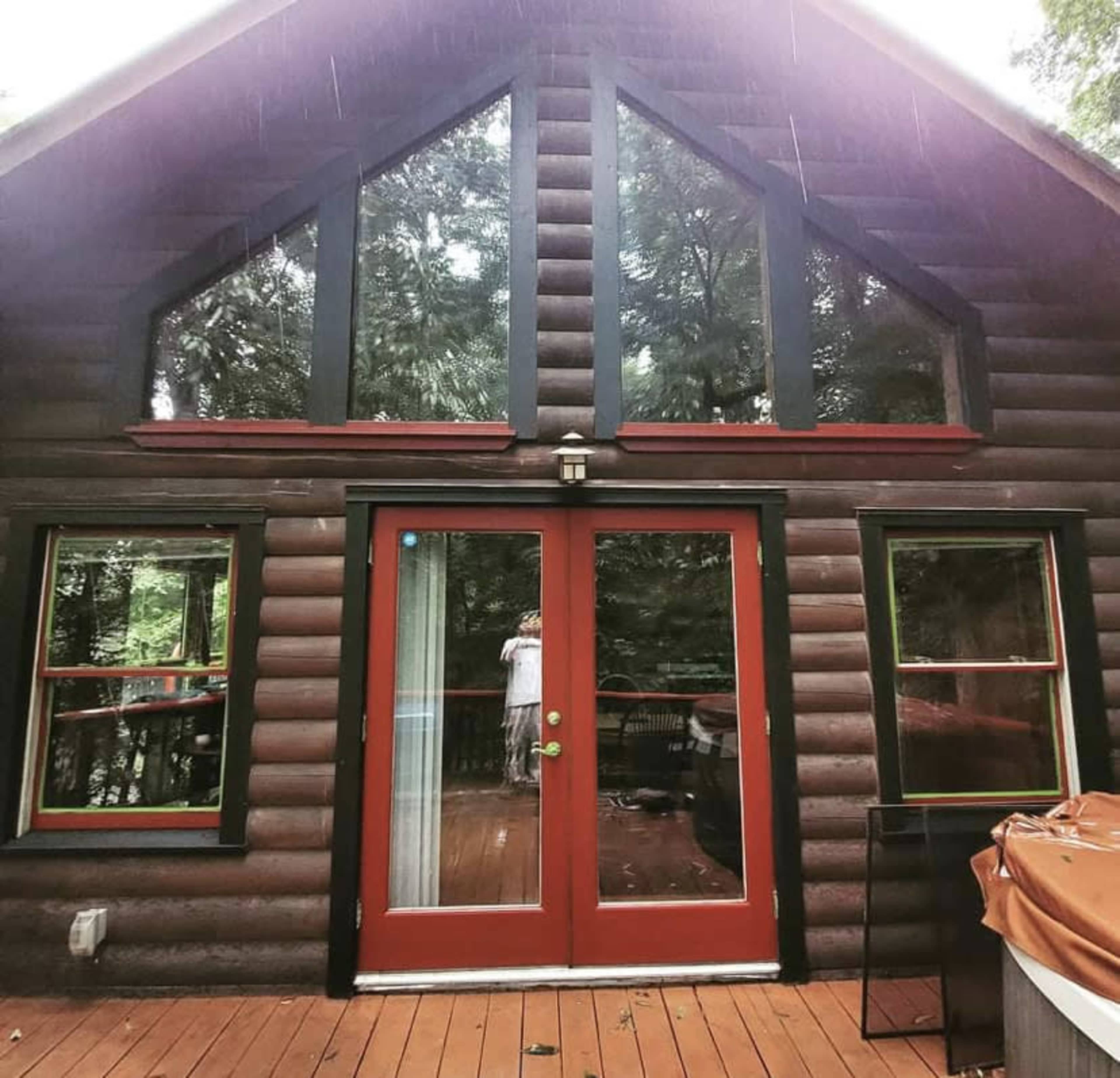A rustic cabin with large windows and a wooden deck is shown under rain.