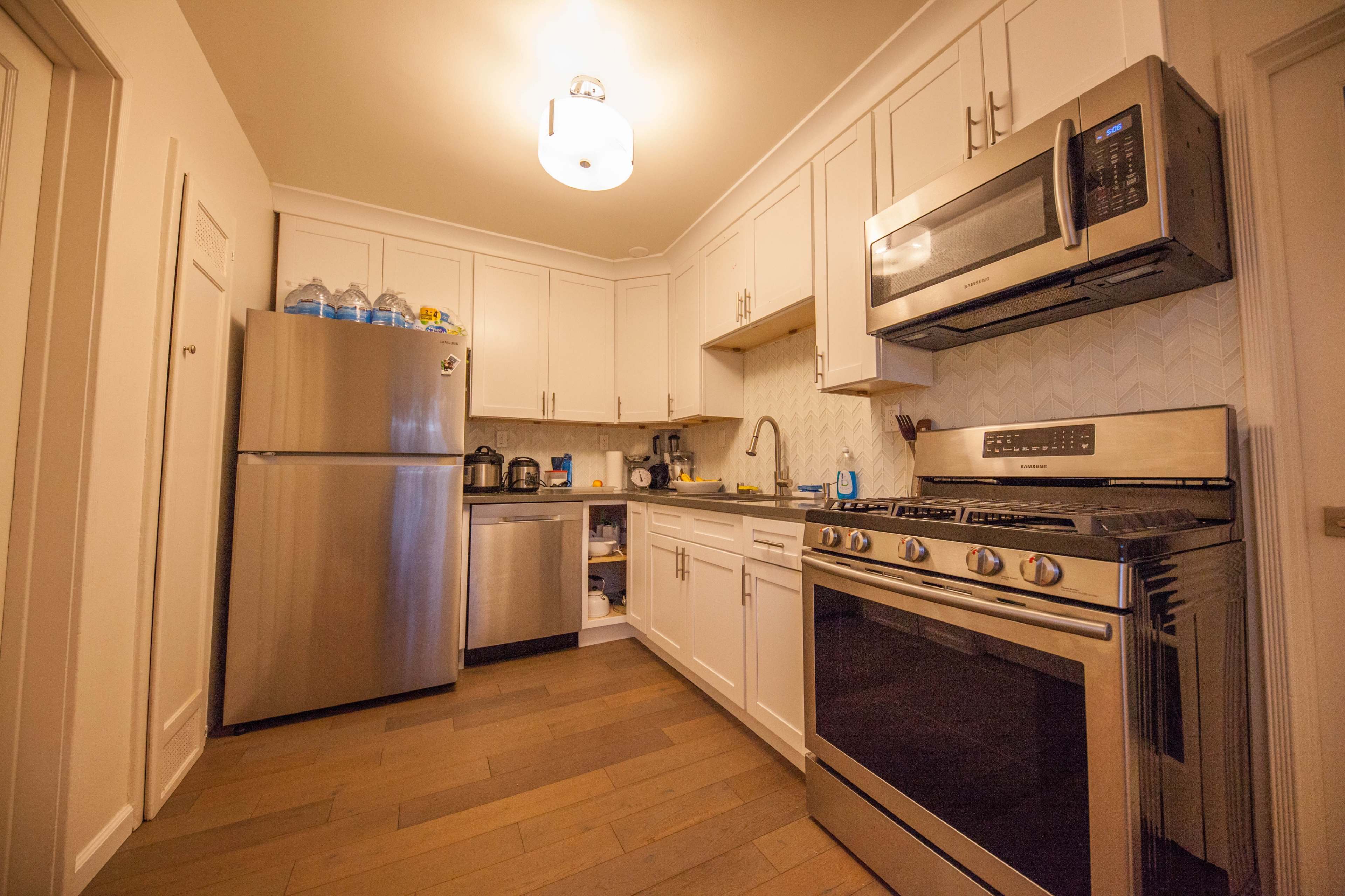 A modern kitchen with stainless steel appliances, white cabinetry, and wooden floors.