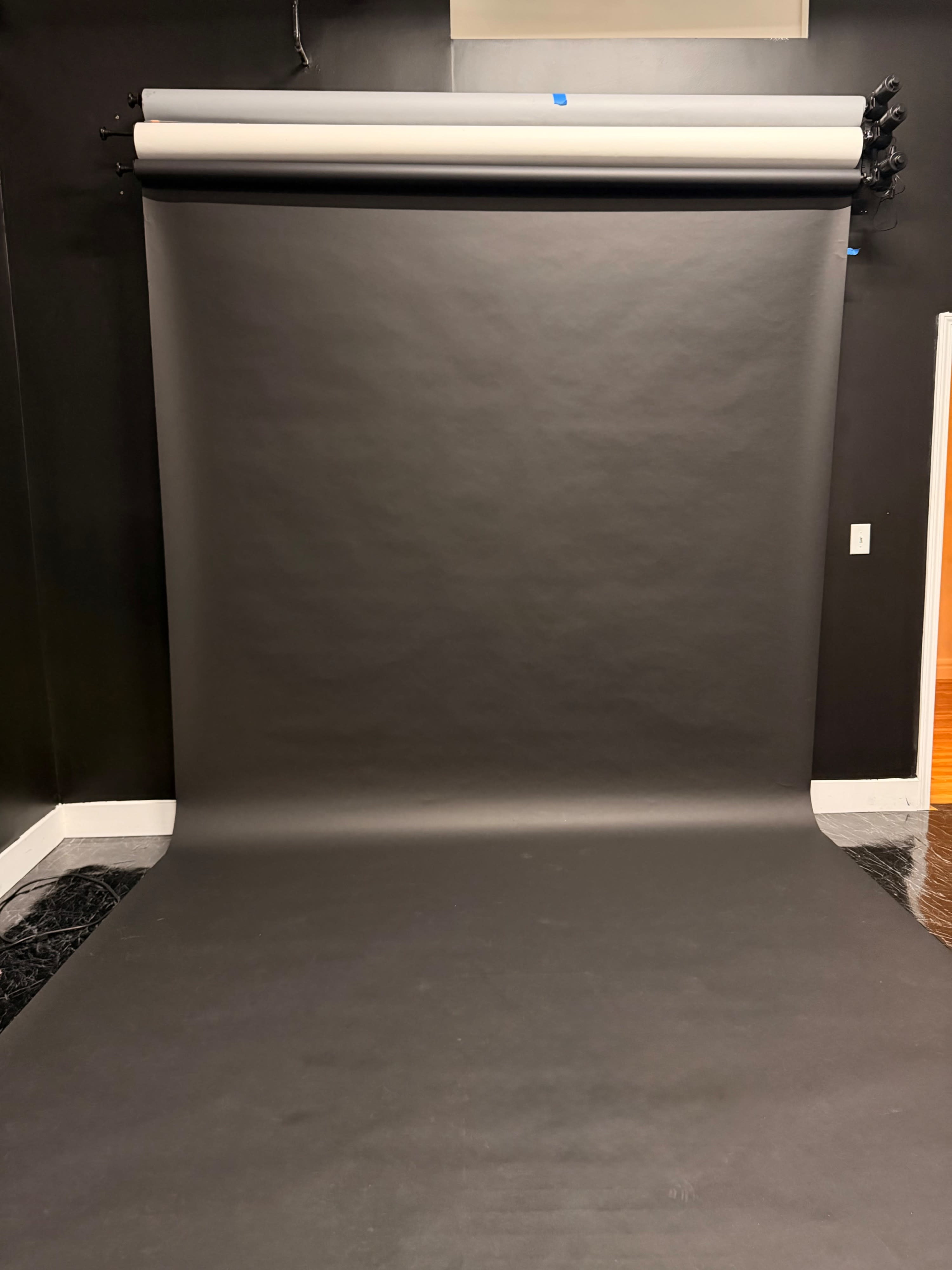 The image shows a black backdrop setup on a wall with a roll of paper hanging above and a smooth, flat surface beneath it.