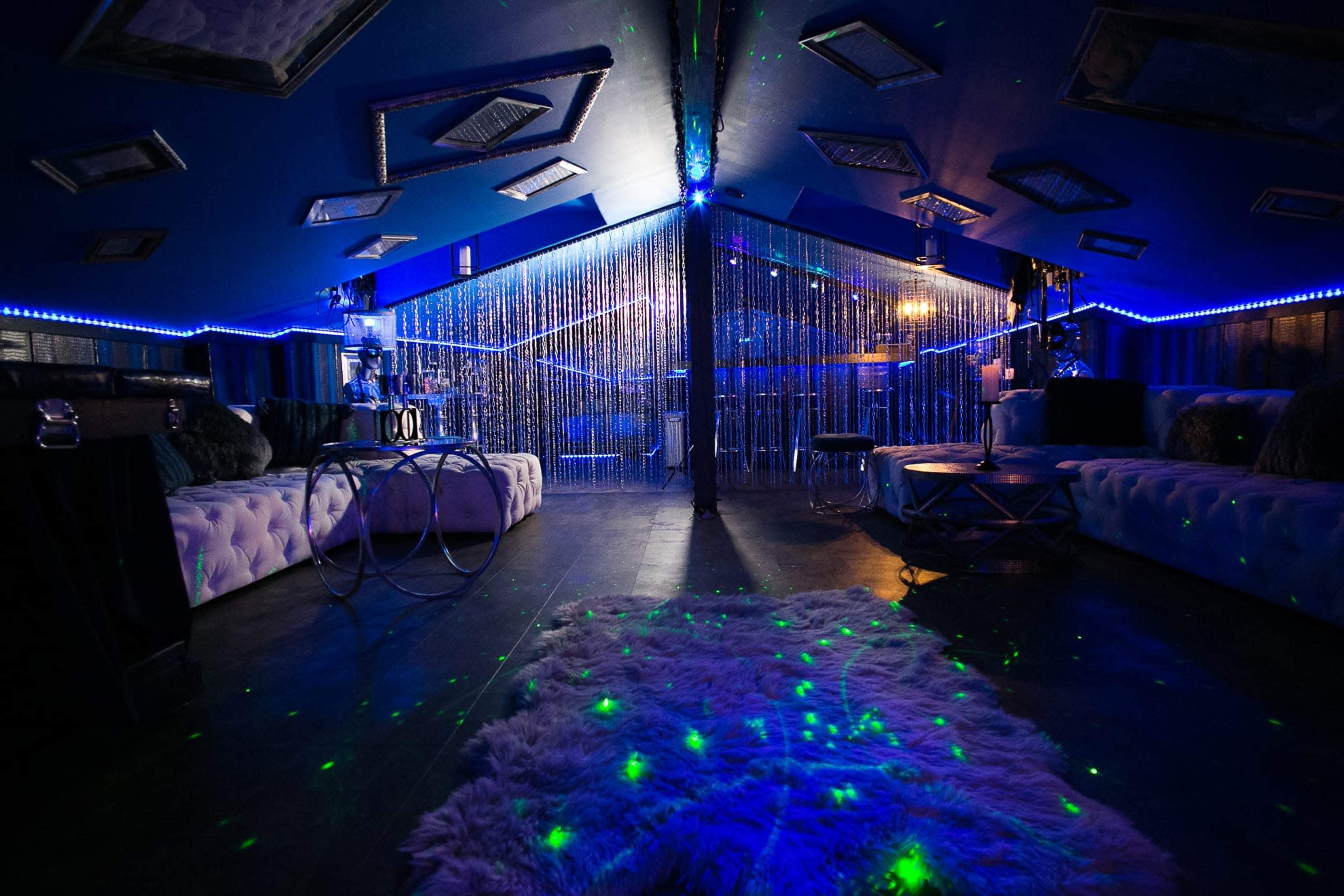 A dimly lit lounge area featuring plush seating, decorative lighting, and a curtain of beads separating different sections.