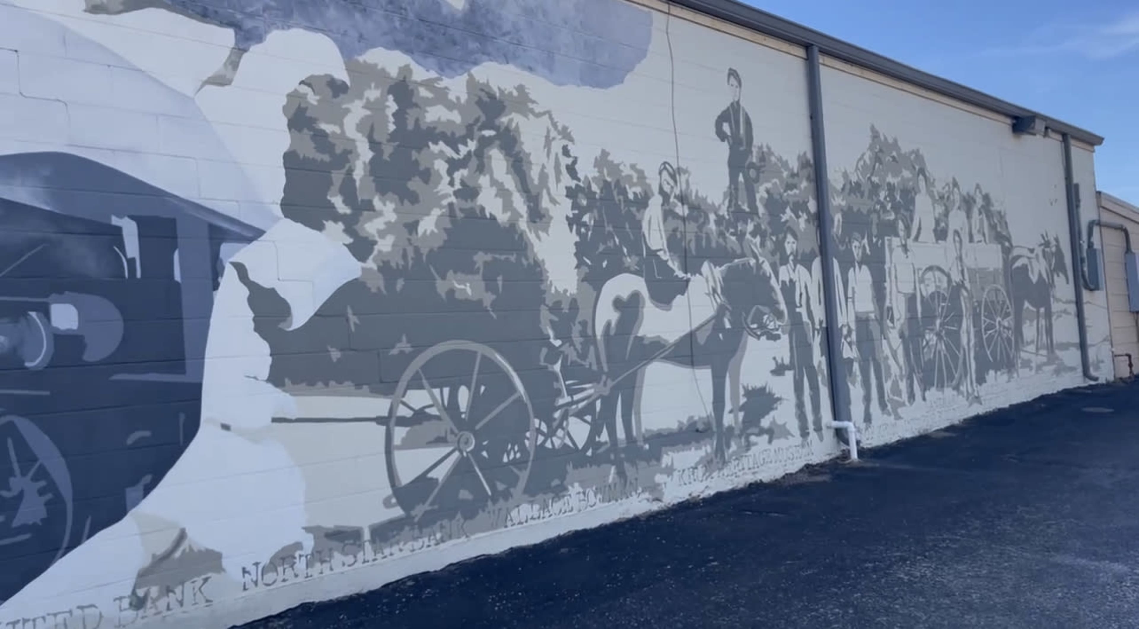 A large grayscale mural depicting scenes of agriculture and transportation, featuring horses and carriages next to a train.