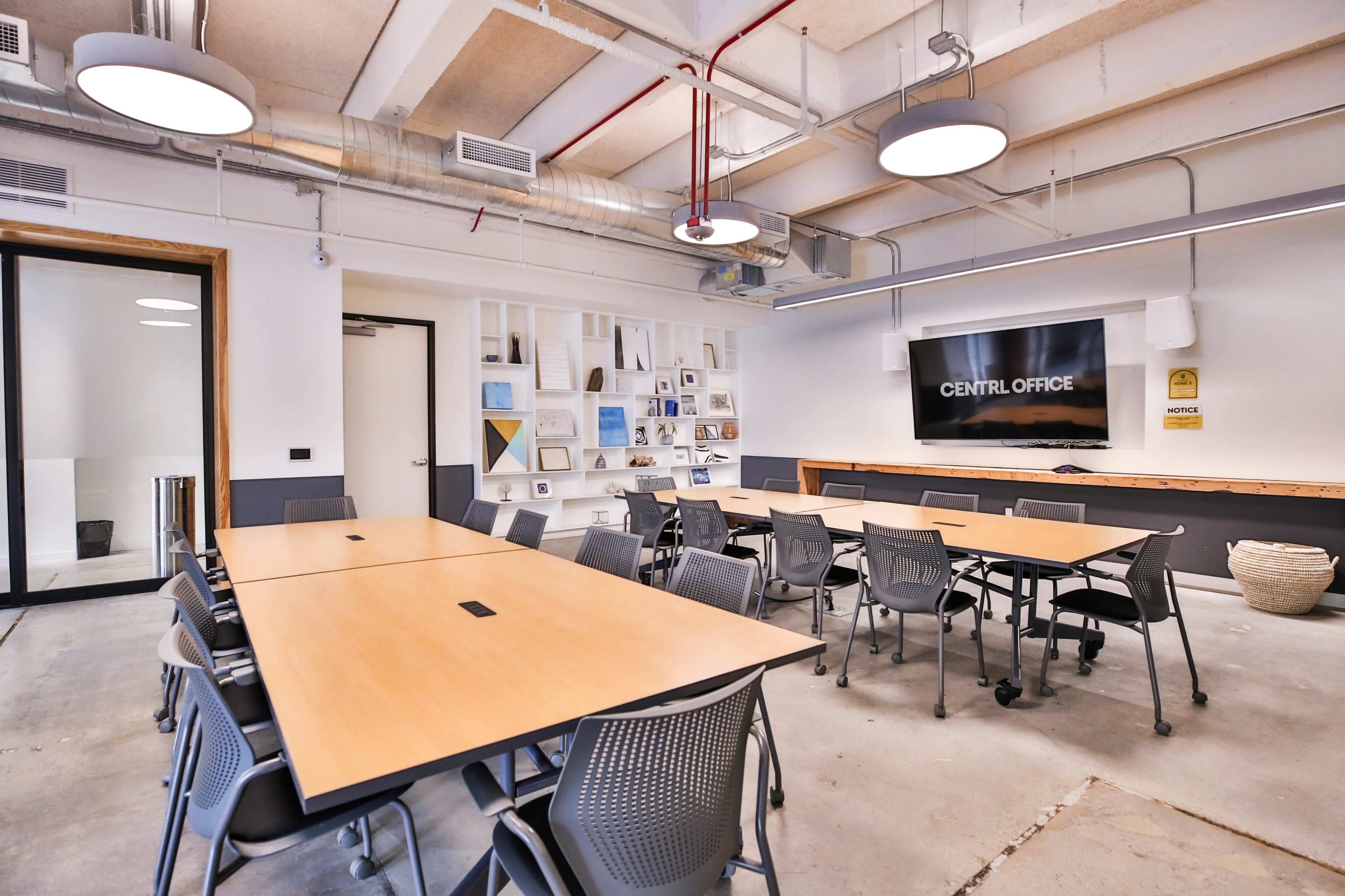 A modern conference room featuring several tables arranged for meetings, with a large screen mounted on the wall and a minimalist decor.