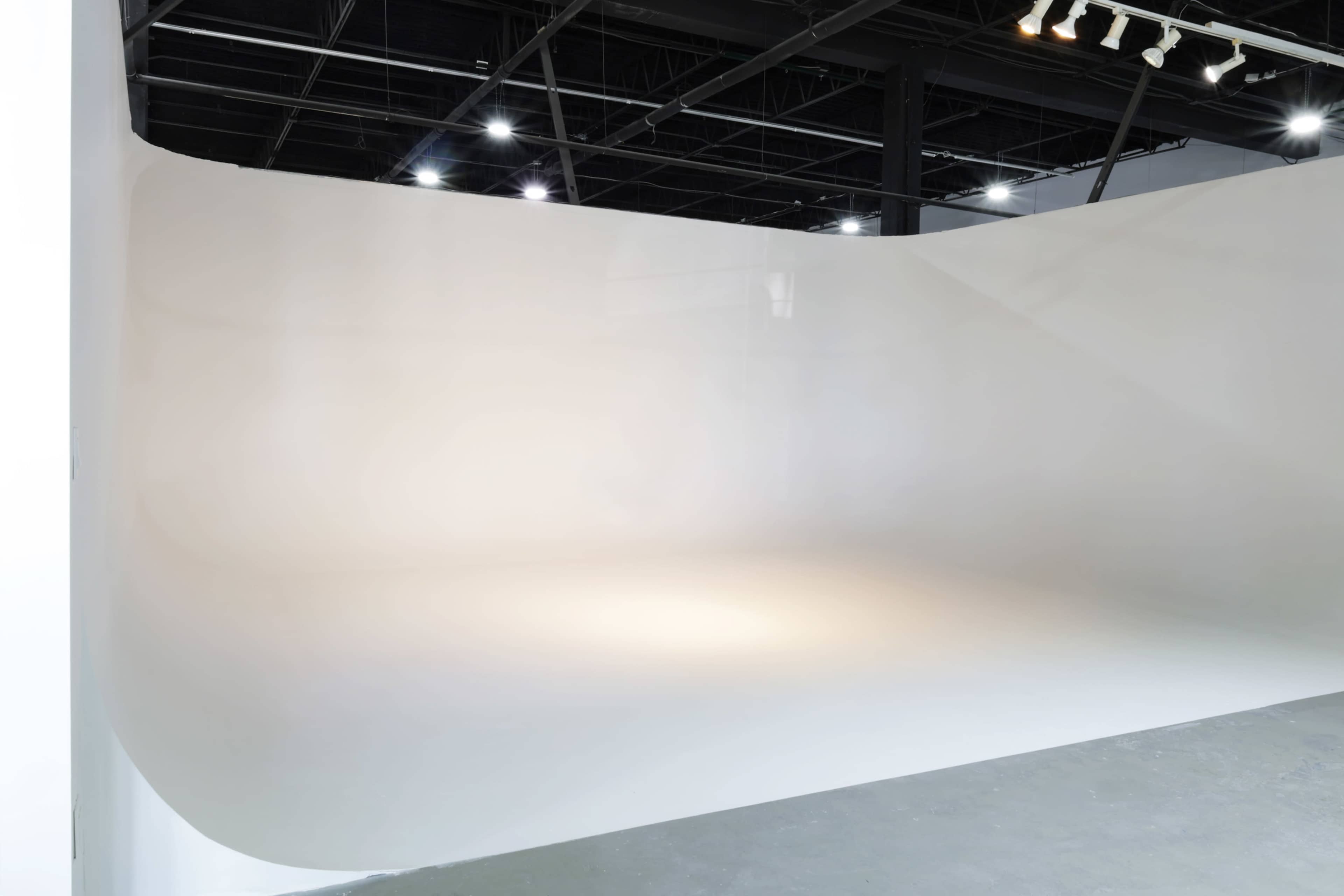 The image depicts a spacious, curved white interior with soft lighting and a smooth floor.