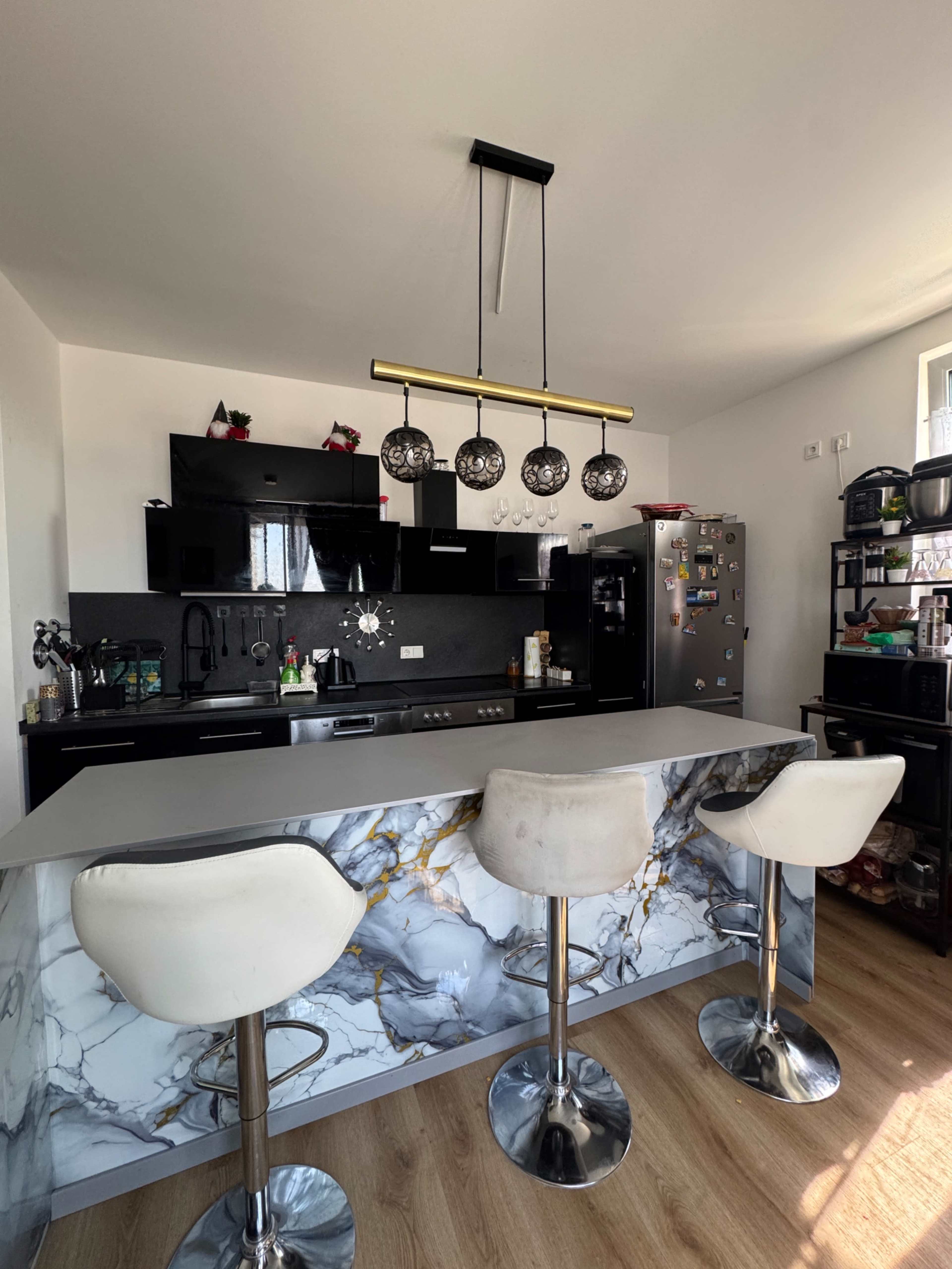The image shows a modern kitchen with a marble-patterned island featuring three white stool chairs, black cabinetry, and a sleek pendant light above.