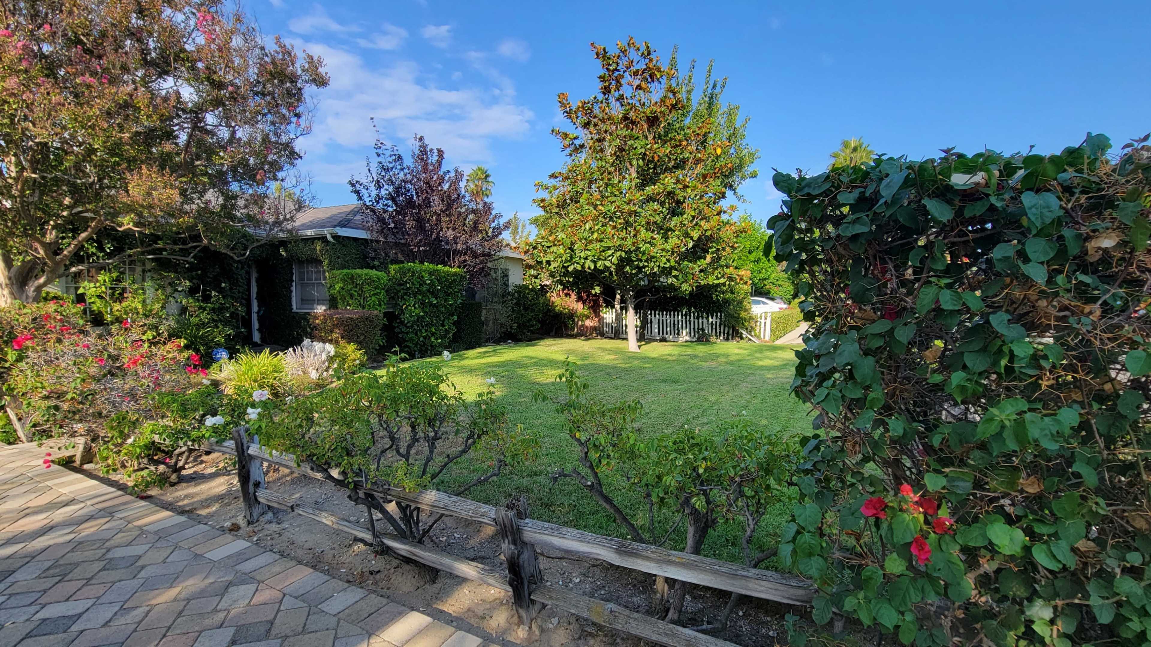A well-maintained garden with grass, surrounded by shrubs and flowering plants, is visible beside a house.