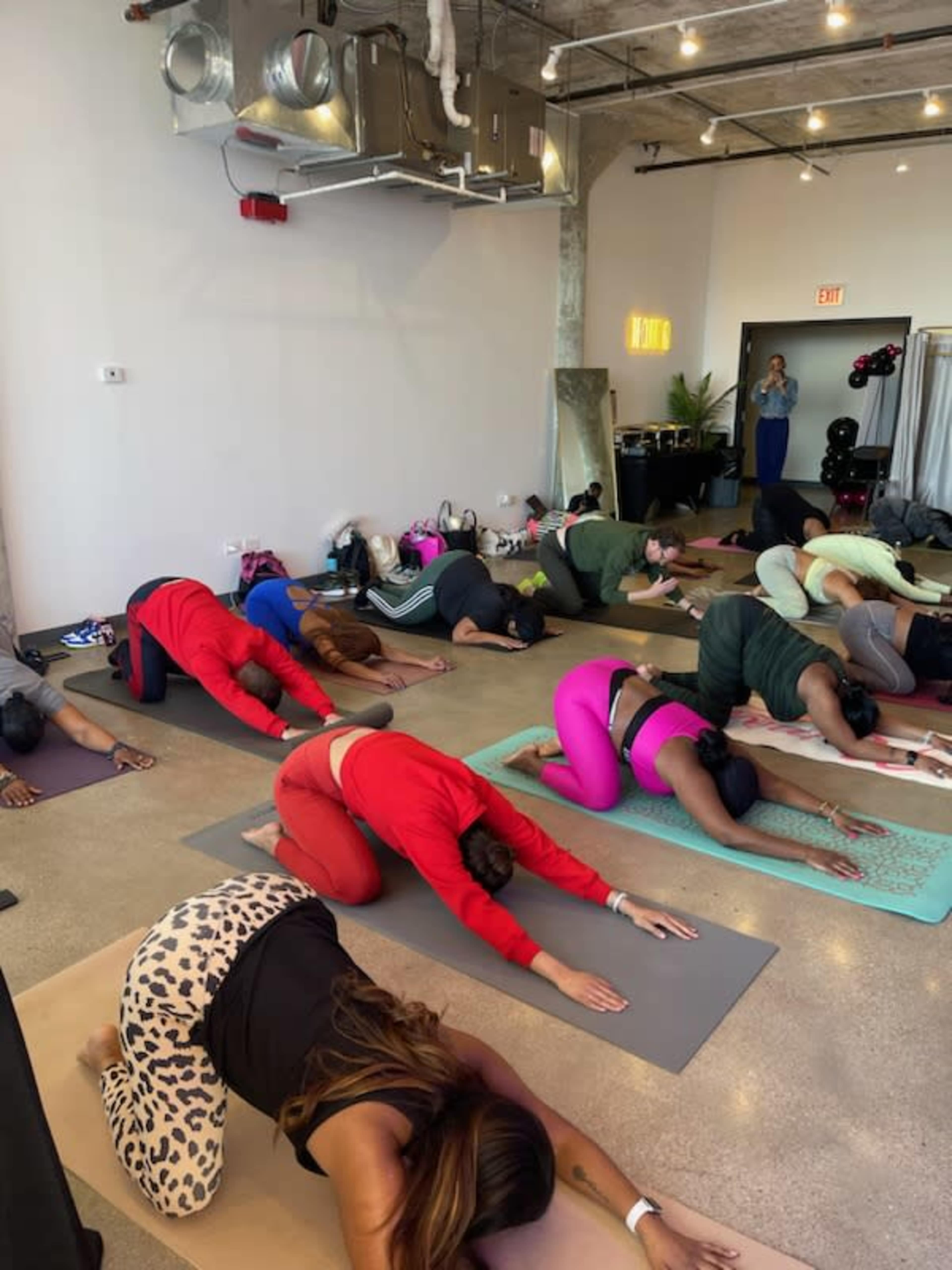 A group of people is participating in a yoga class, performing a child’s pose on yoga mats in a studio.
