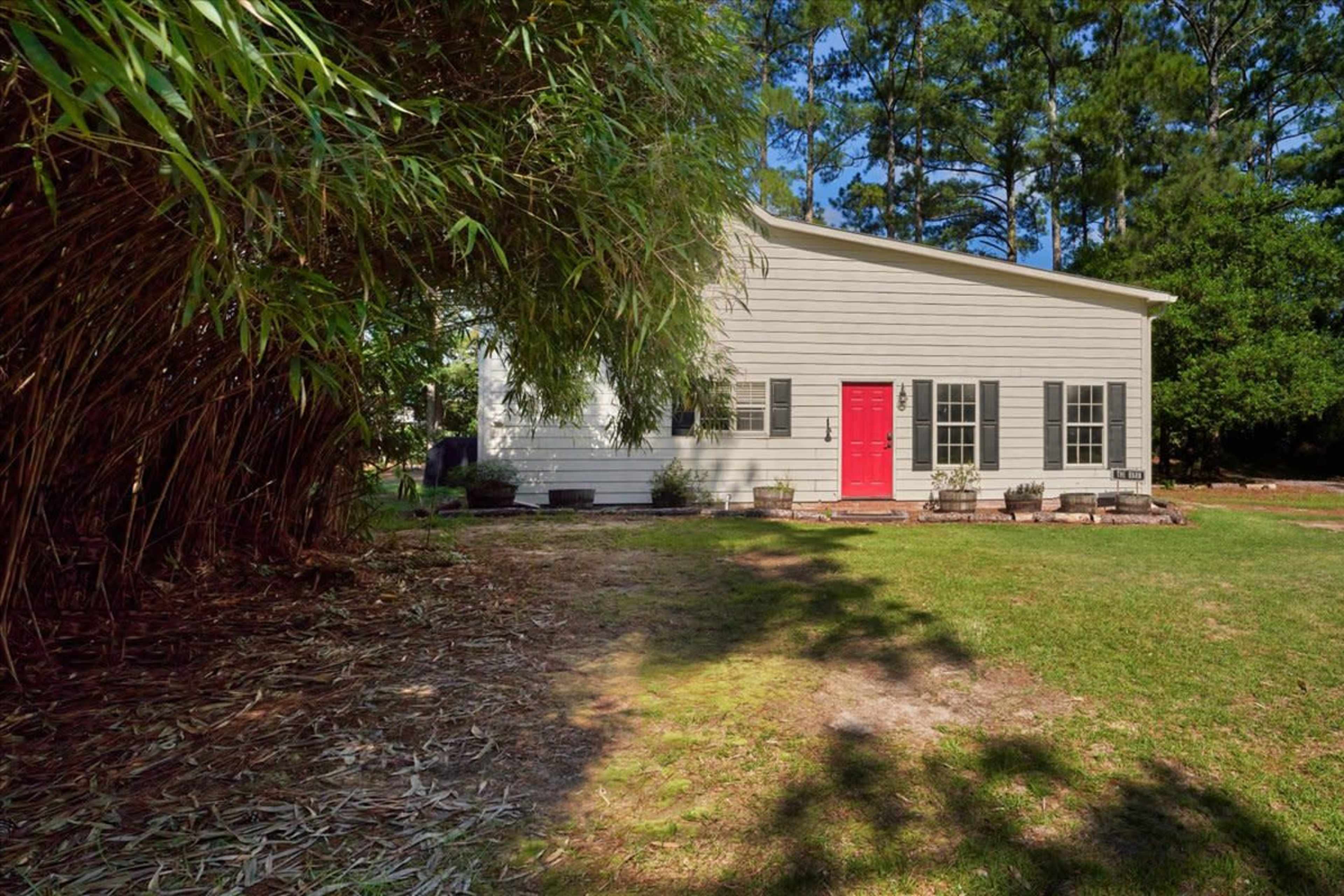 A two-story wooden house with a red front door is surrounded by tall green bamboo and trees.