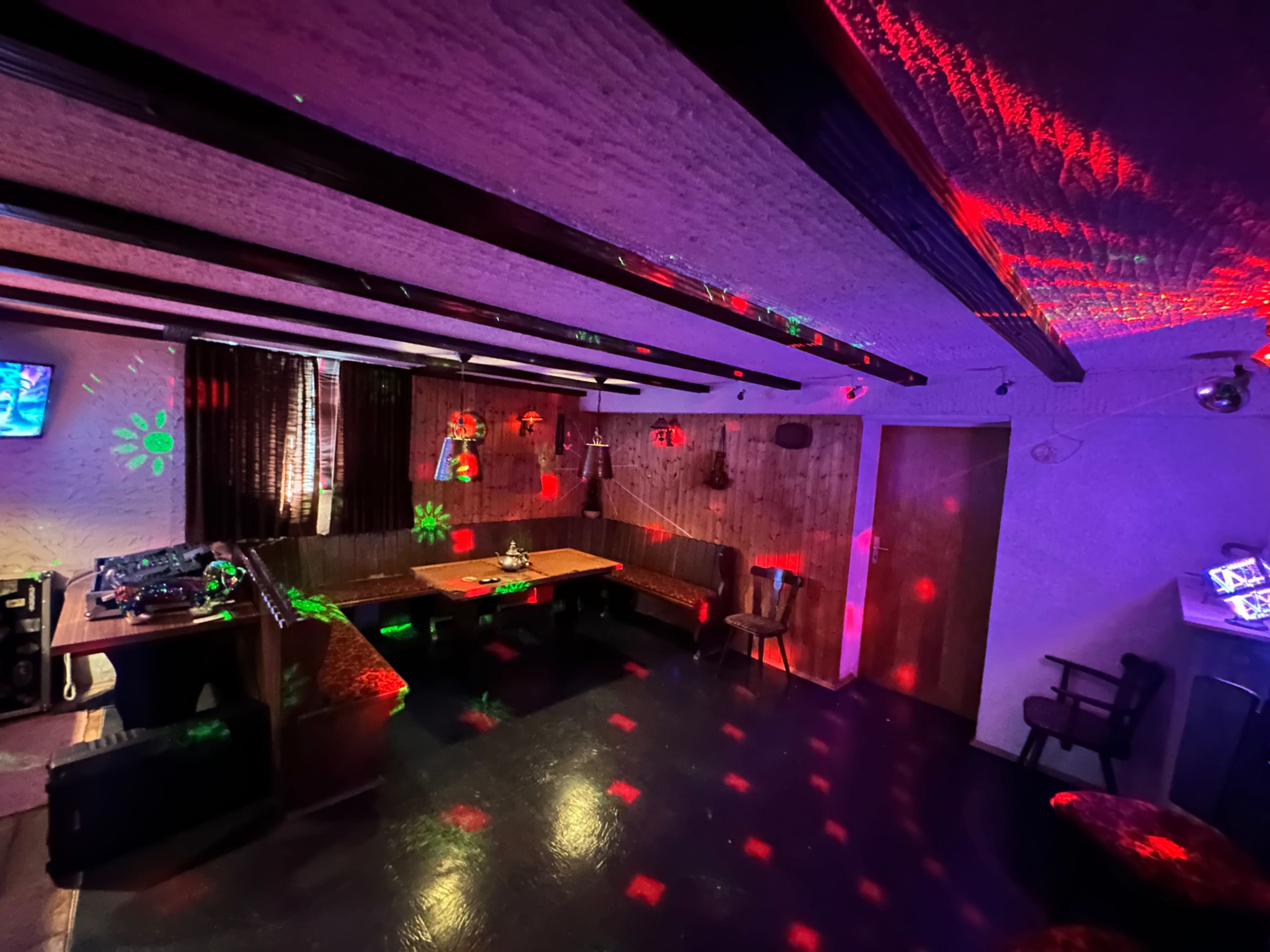 A dimly lit room with a large table and seating, decorated with colorful light projections on the walls and ceiling.