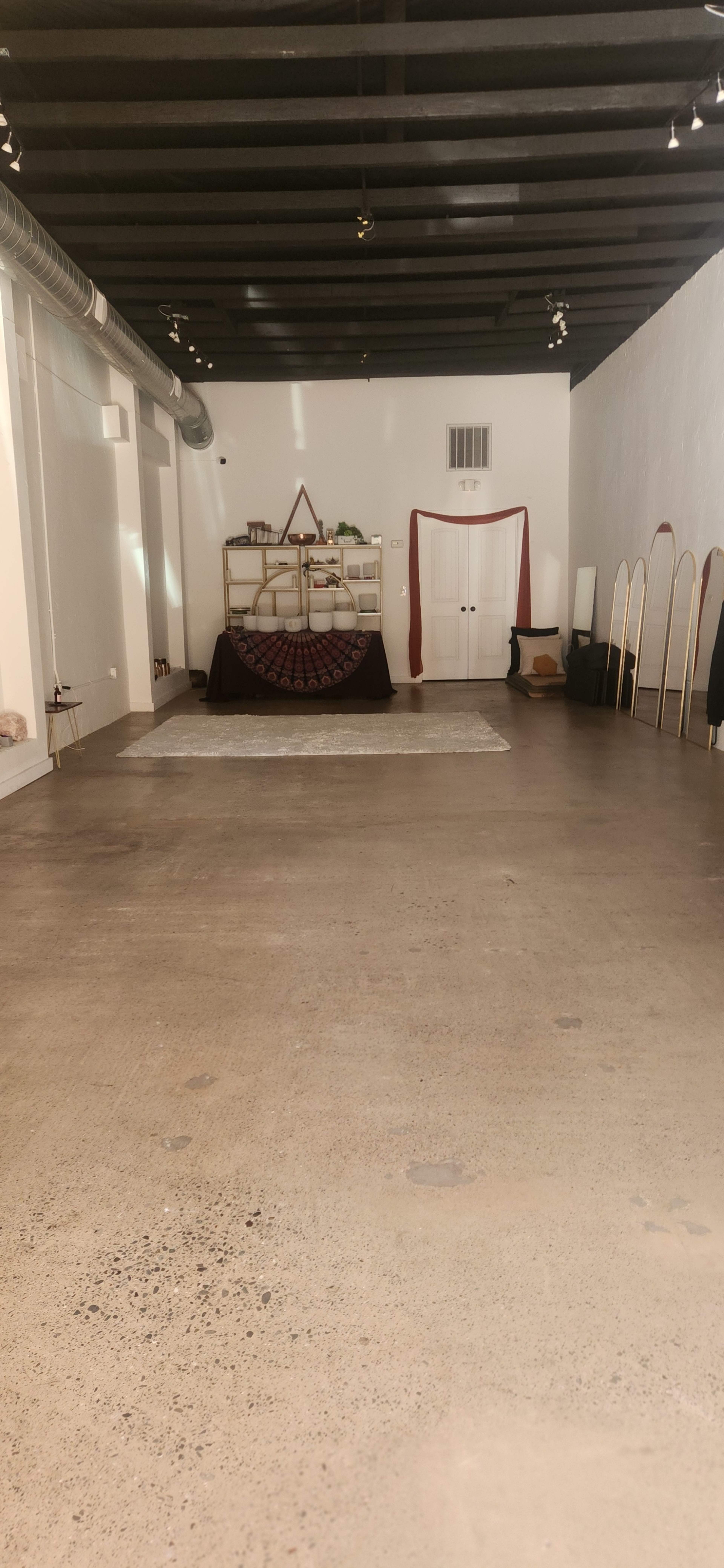 The image shows a spacious interior with polished concrete floors, featuring a central display area with a circular decorative item, a storage shelf, and several mirrors along the back wall.