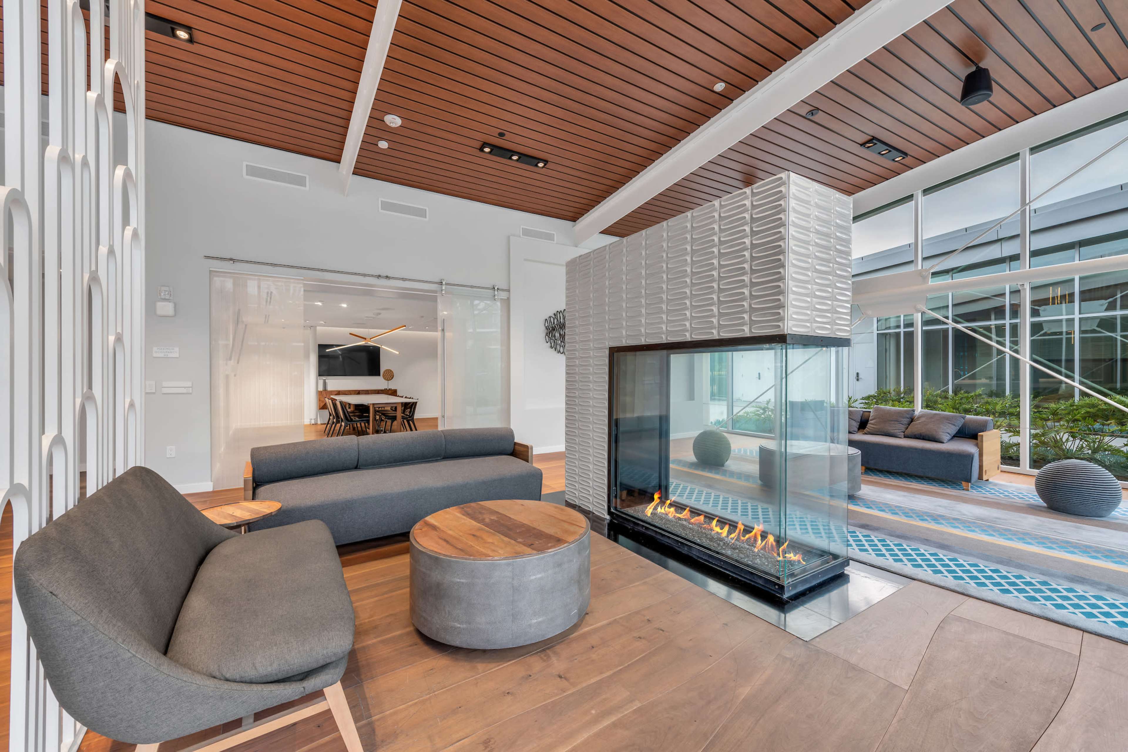 A modern, open living space featuring a glass-enclosed fireplace, contemporary seating, and a dining area with large windows.