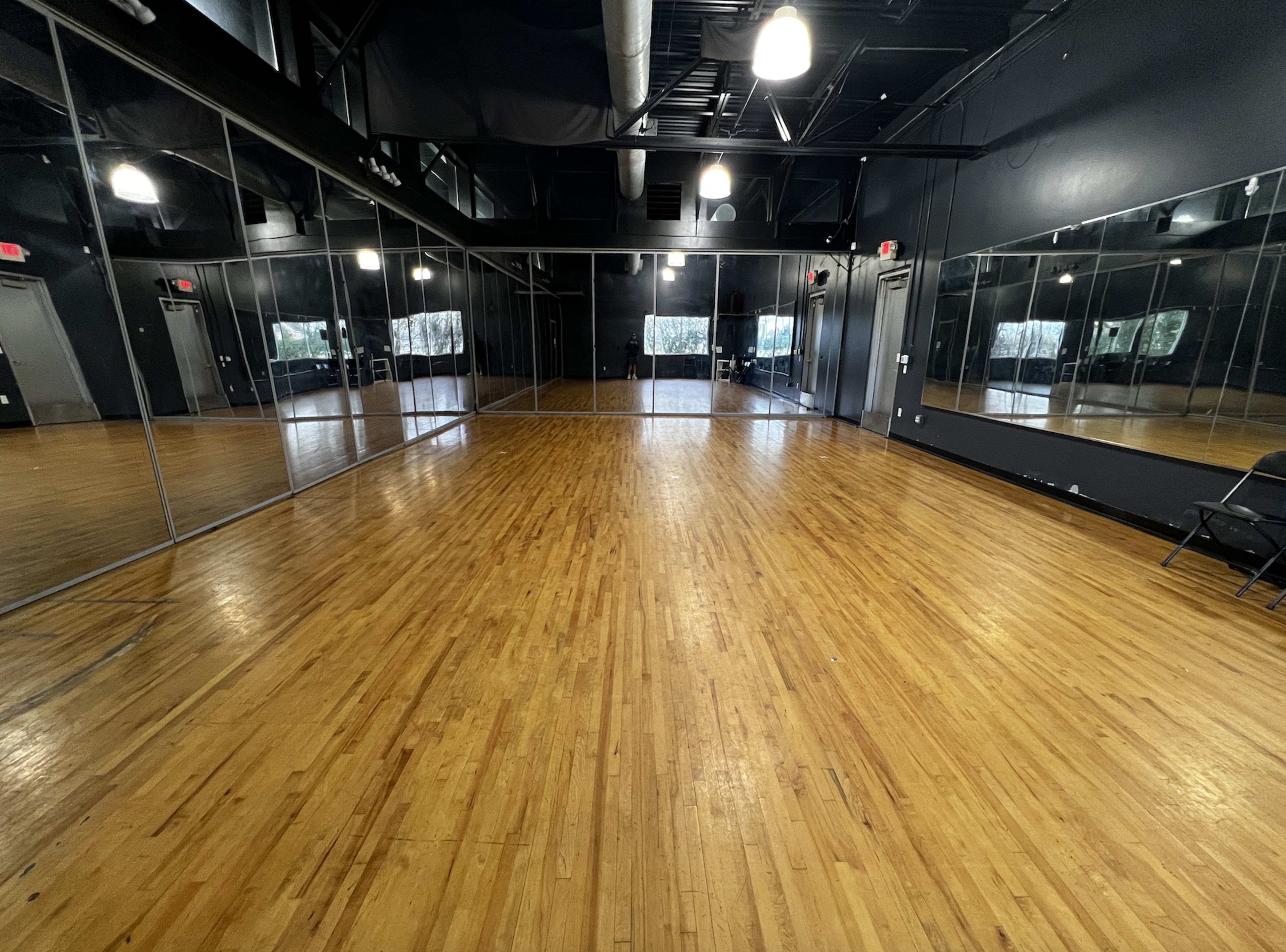 A spacious dance studio with wooden floors and large mirrors lining the walls.