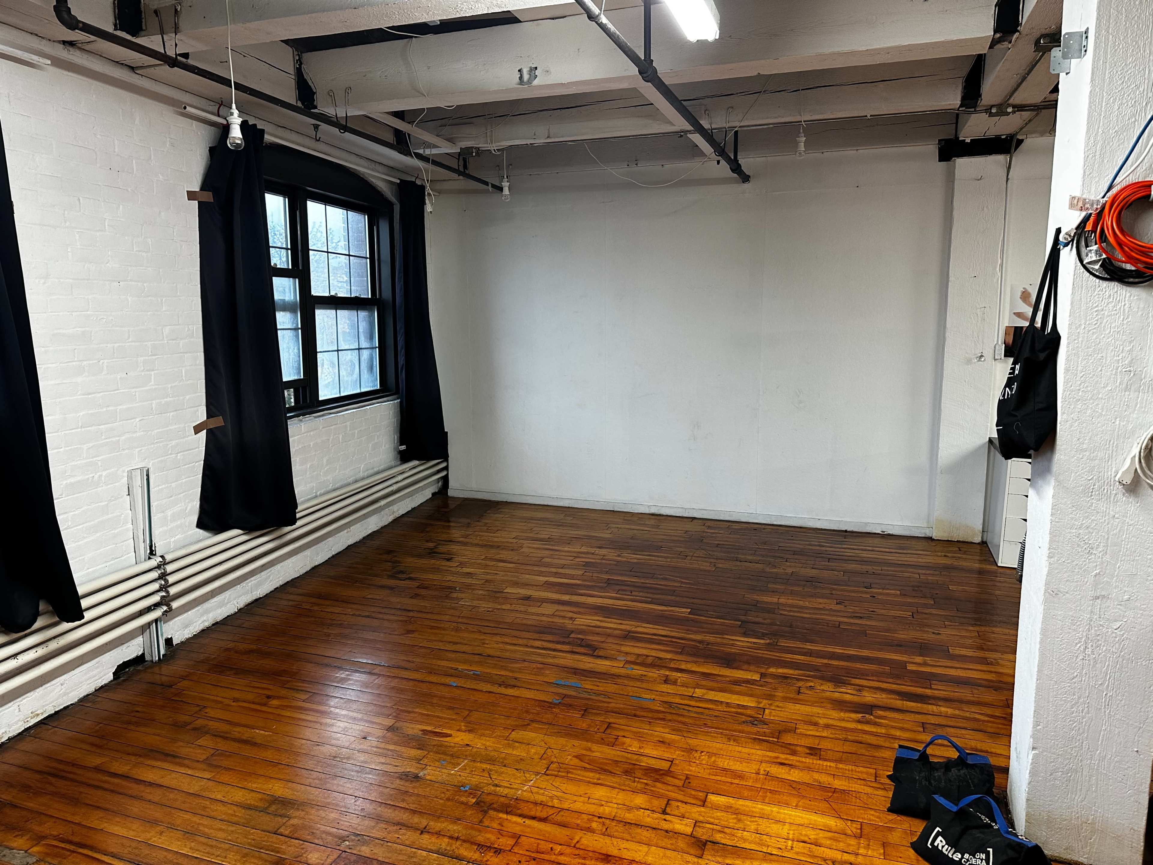 An empty room with wooden flooring, white walls, and a window covered by black curtains.